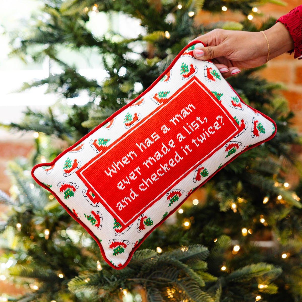 Decorative pillow with humorous text held in front of a Christmas tree
