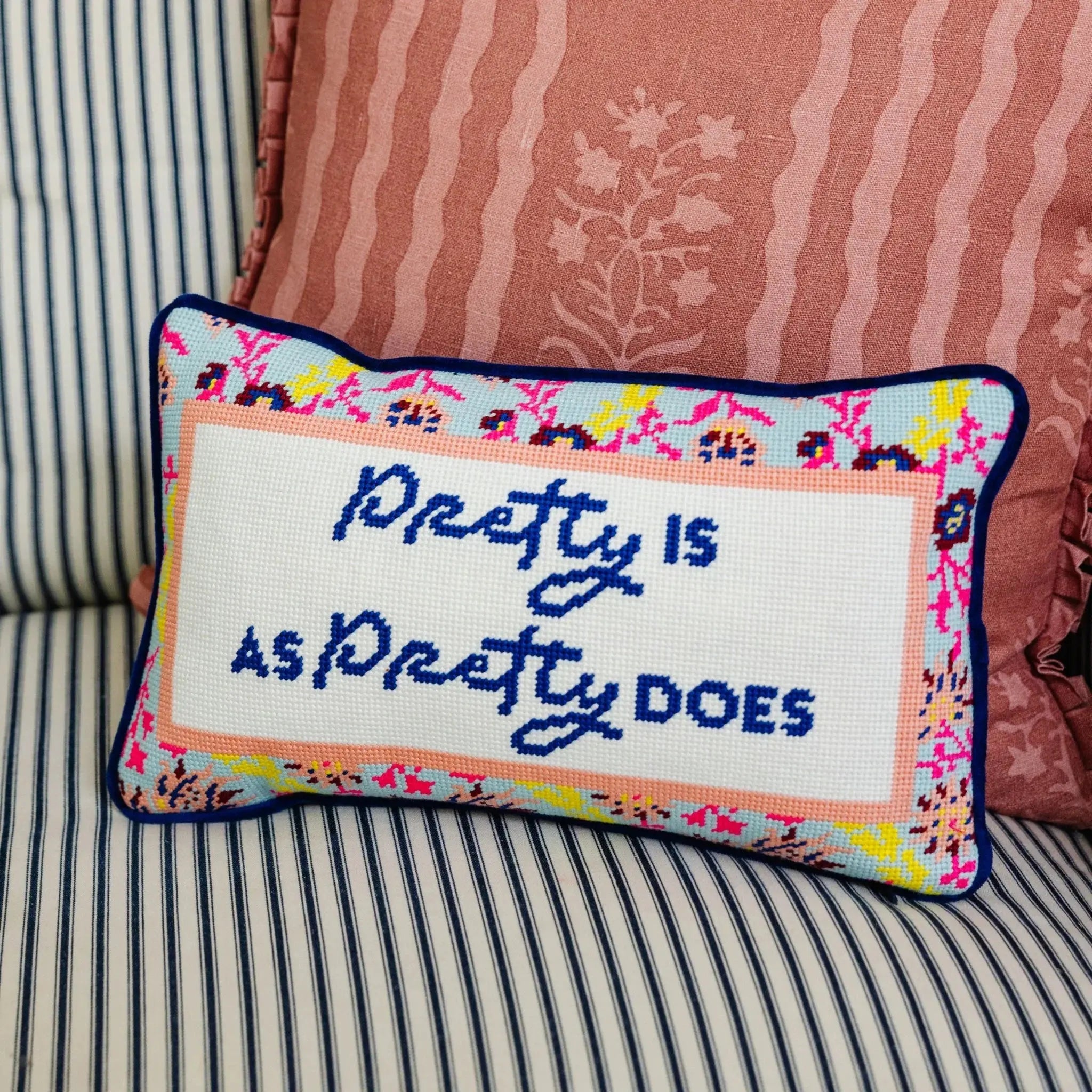Decorative pillow with text "Pretty is as Pretty Does" on a striped couch