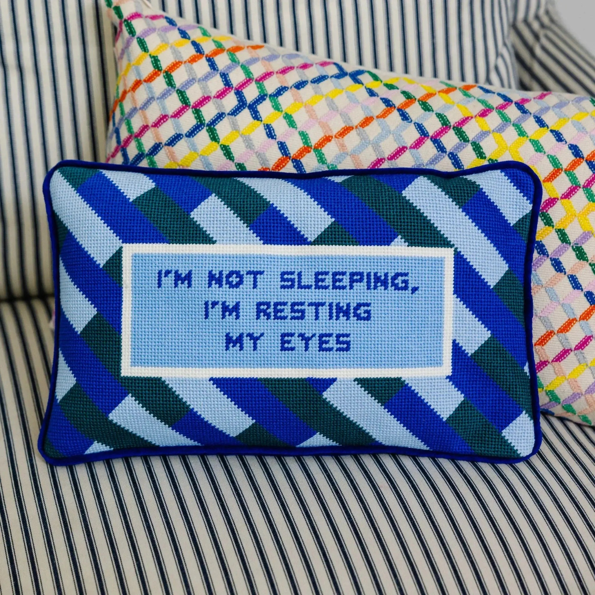 Decorative pillow with text 'I'm not sleeping, I'm resting my eyes' on a striped couch.