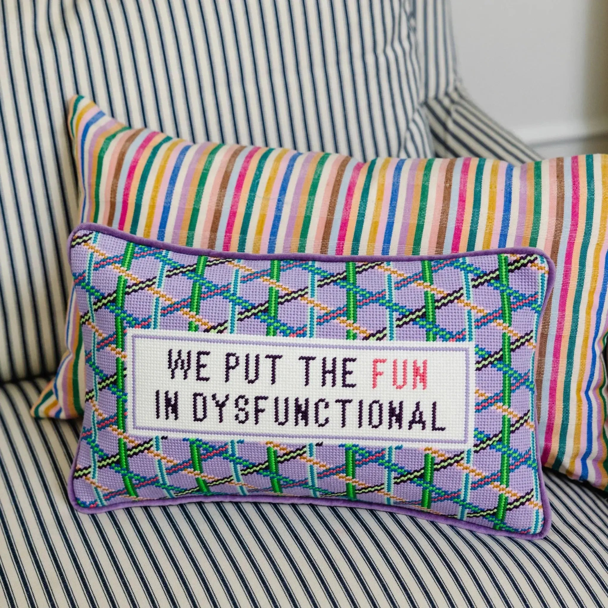 Decorative pillow with colorful striped back and embroidered text on a striped couch.