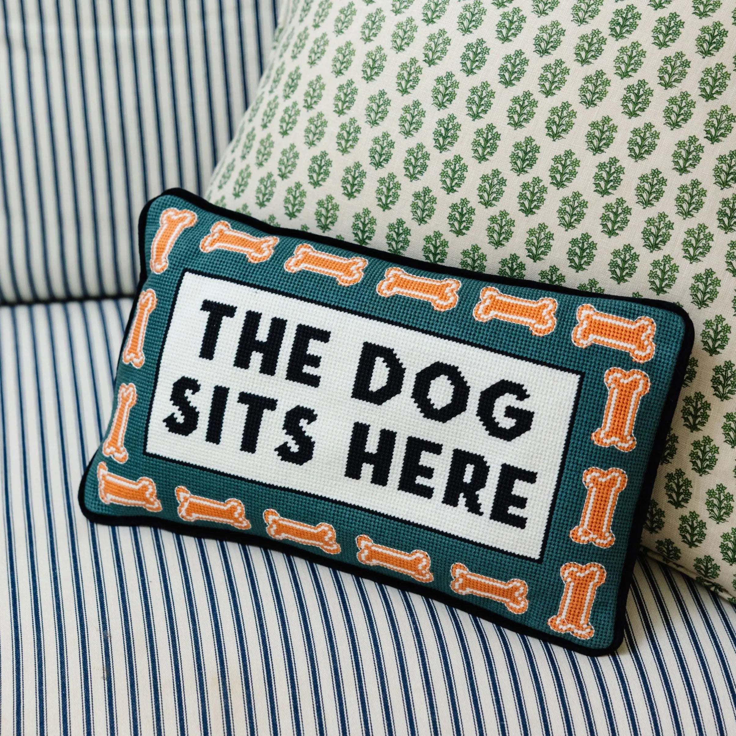 Decorative pillow with 'The Dog Sits Here' text on a striped sofa.