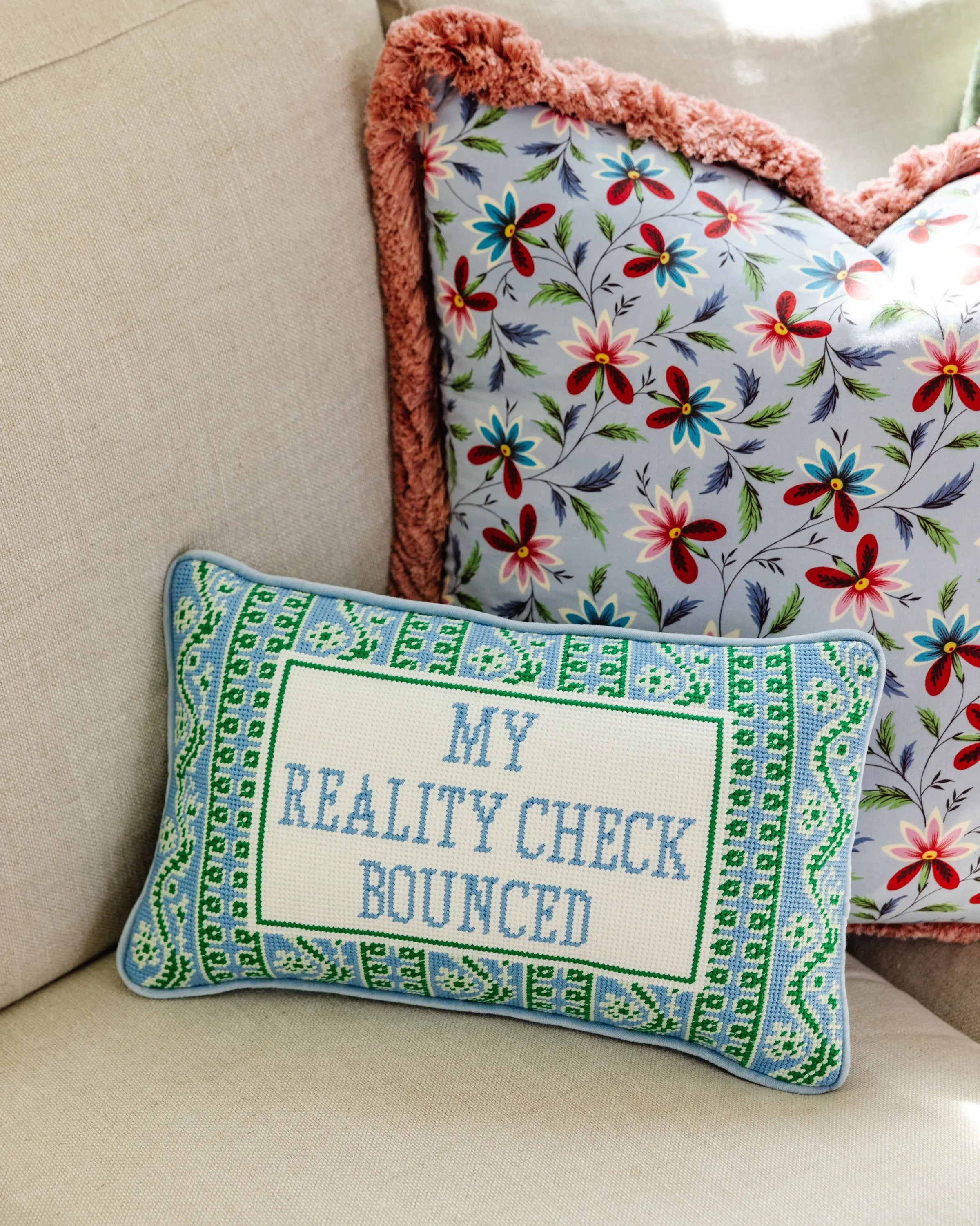 Decorative pillow with floral pattern and embroidered text on a beige couch.