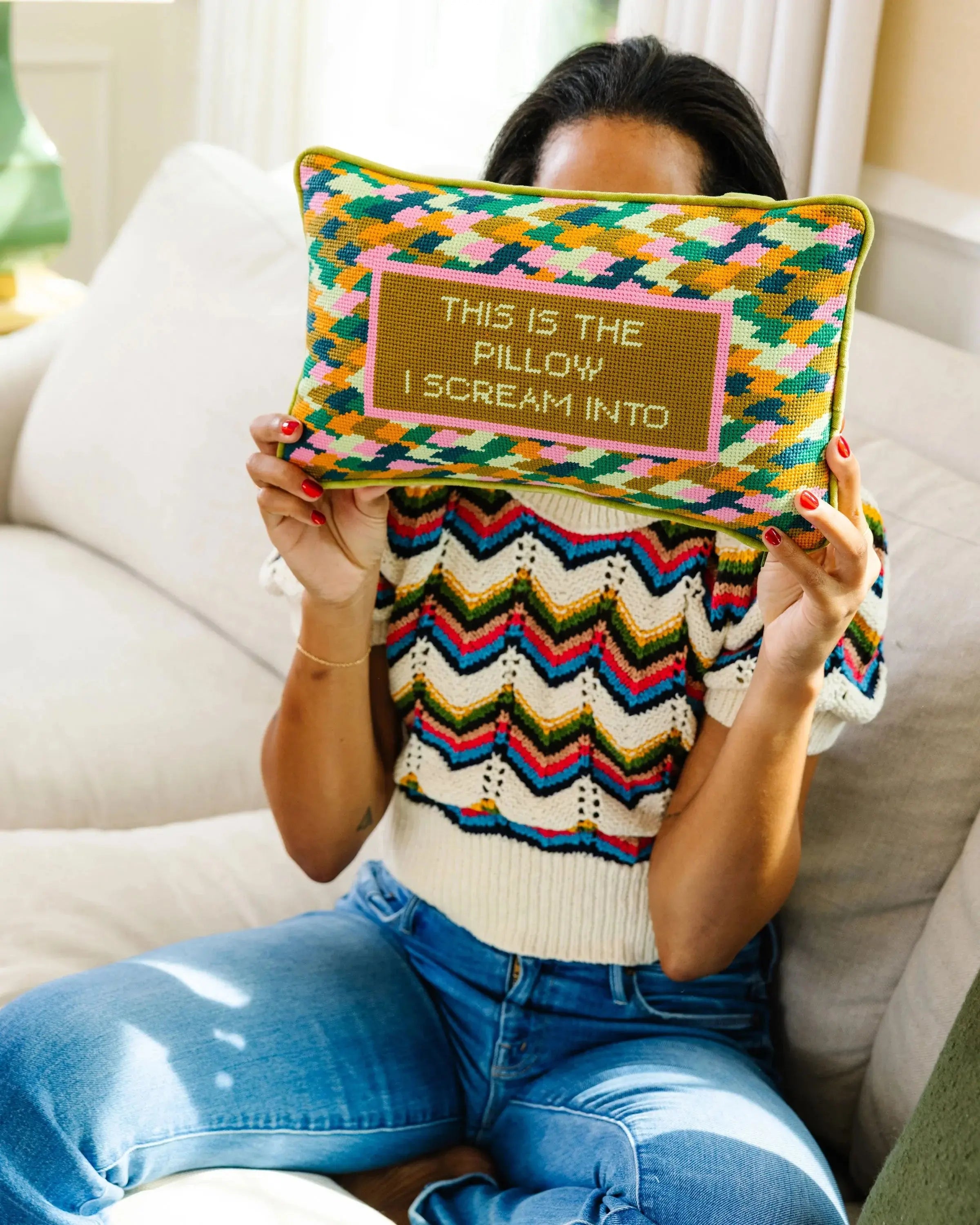Person holding a colorful pillow with text, sitting on a couch.