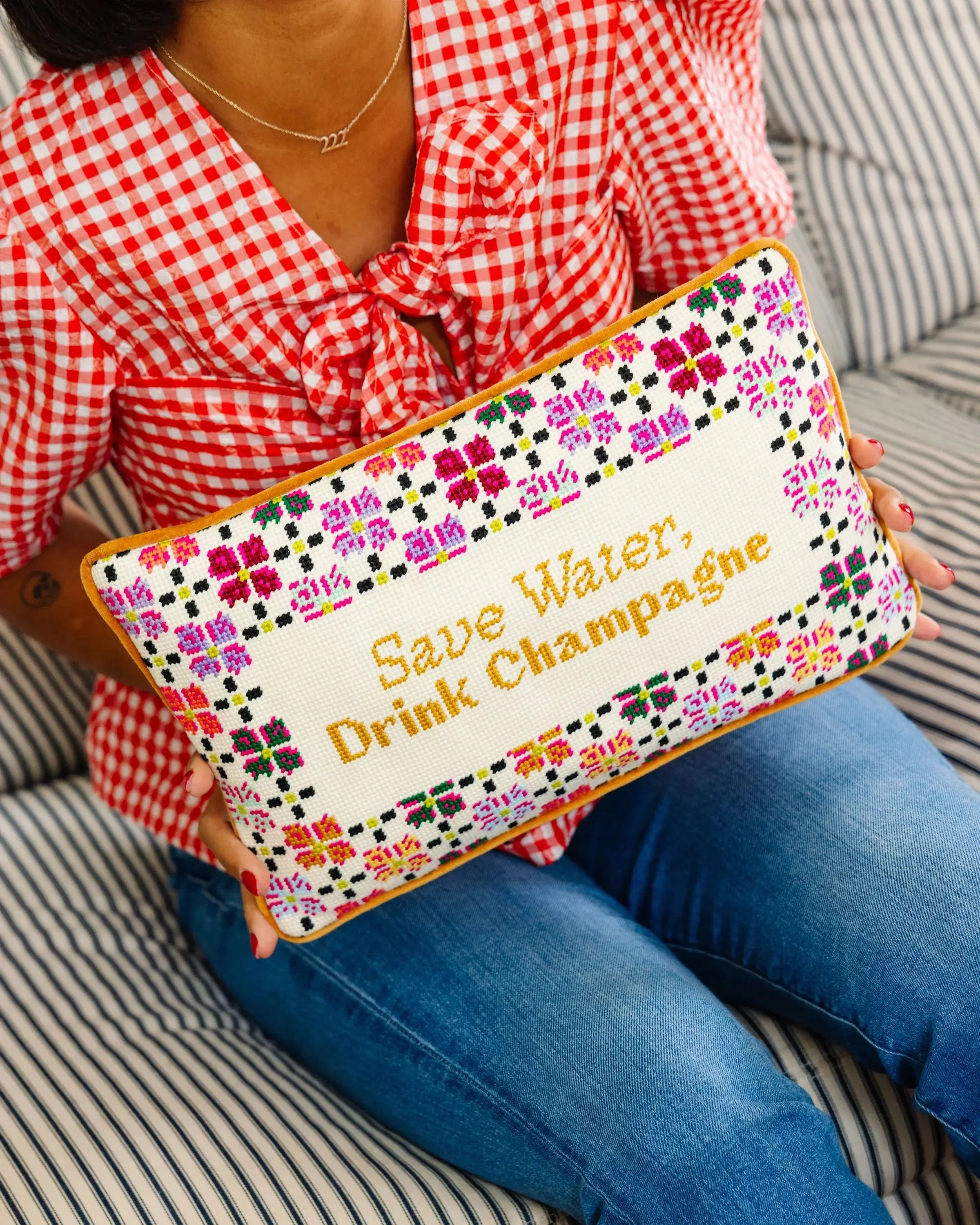Person holding a colorful pouch with text 'Save Water, Drink Champagne' on a striped couch.