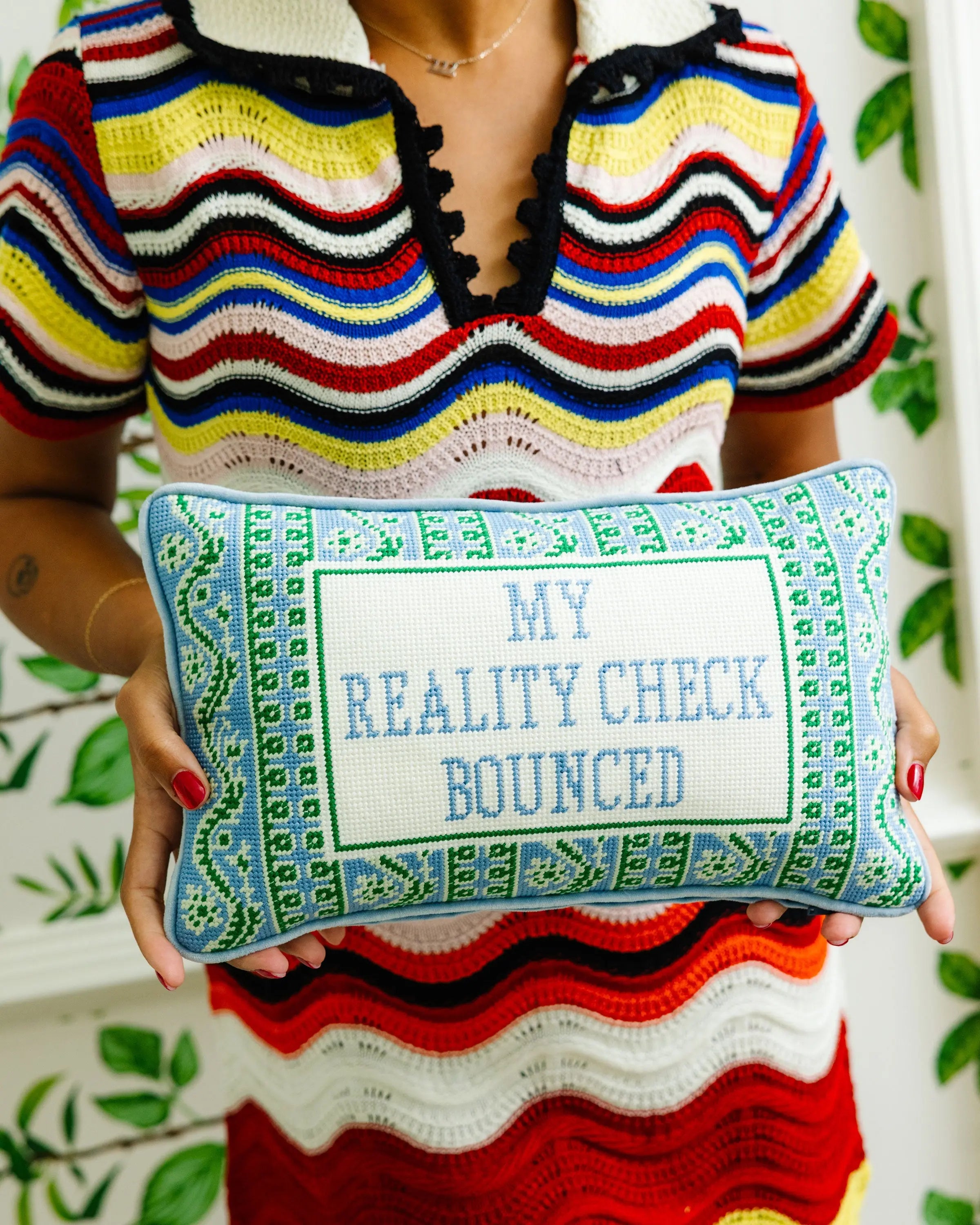 Person holding a pillow with 'My Reality Check Bounced' text against a patterned background