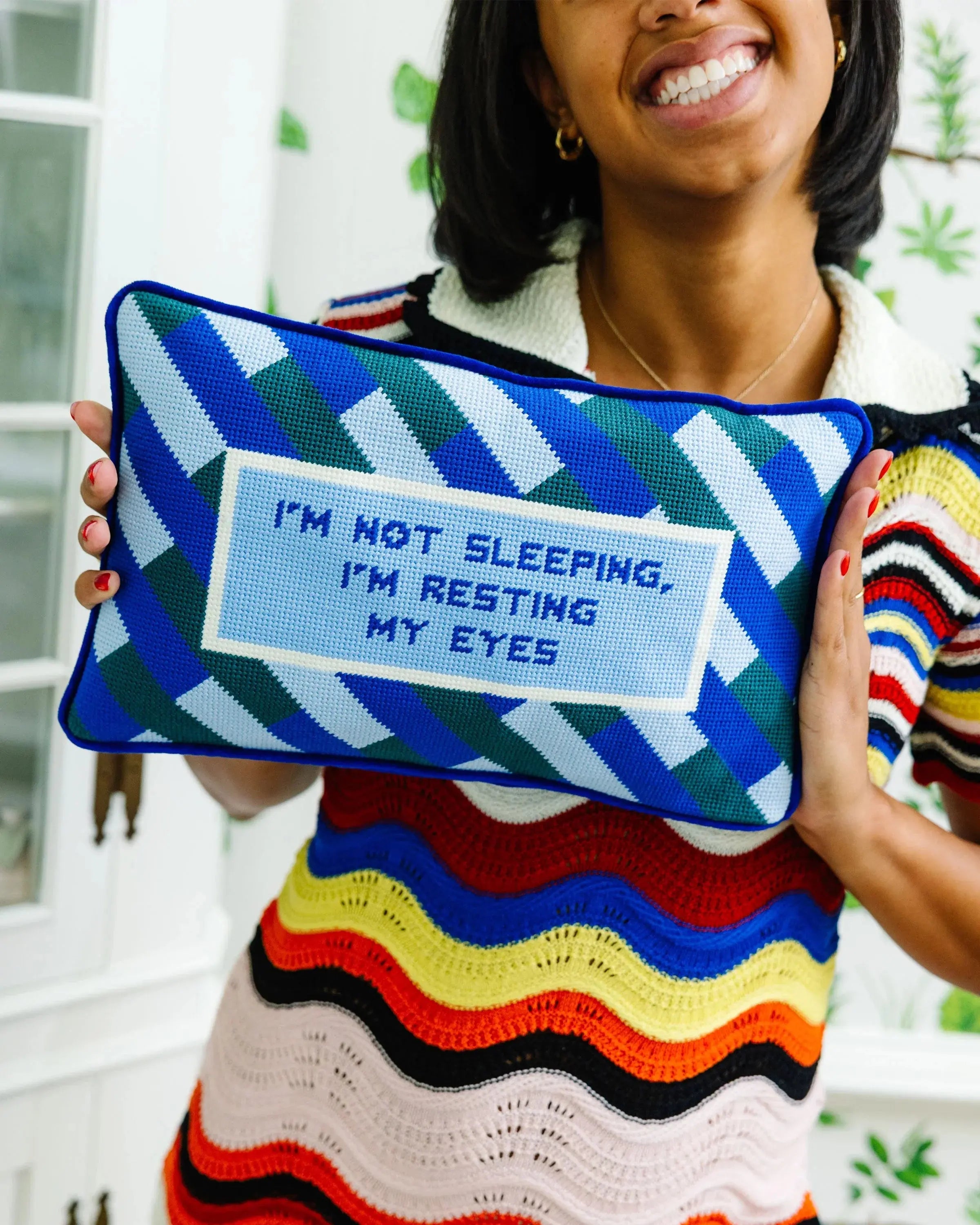 Person holding a colorful pillow with text, wearing a striped sweater.