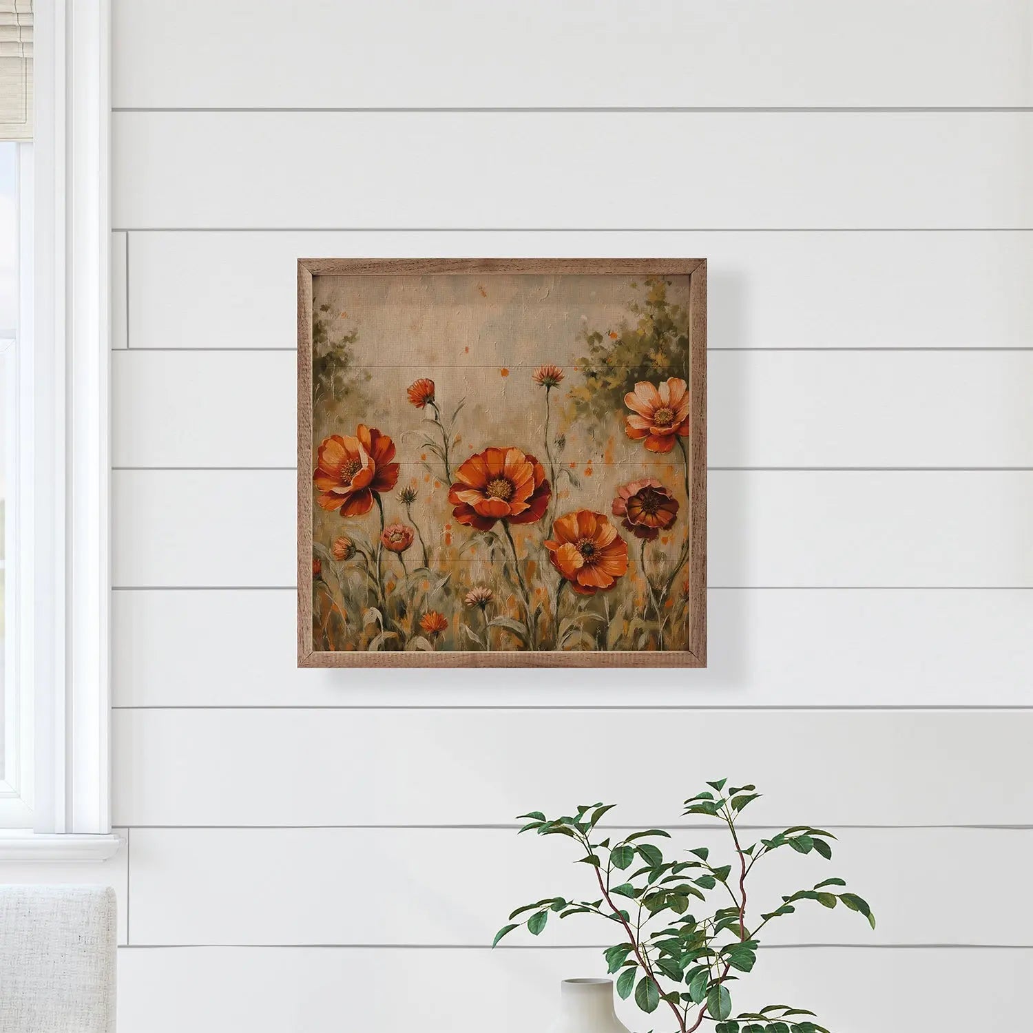 Framed floral painting on a white wall with a plant in the foreground