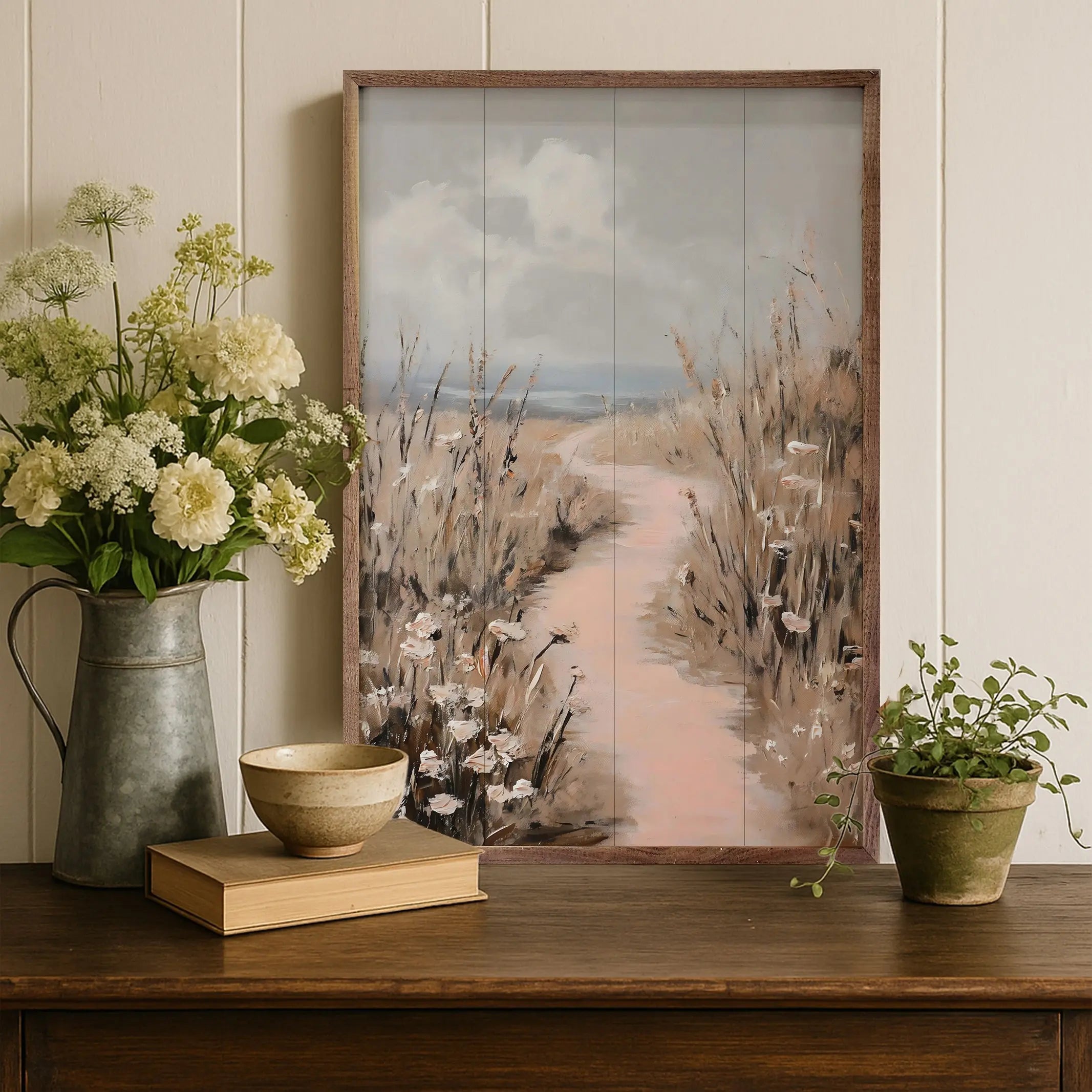 Decorative setup with a framed artwork, flowers, bowl, and plants on a wooden surface.