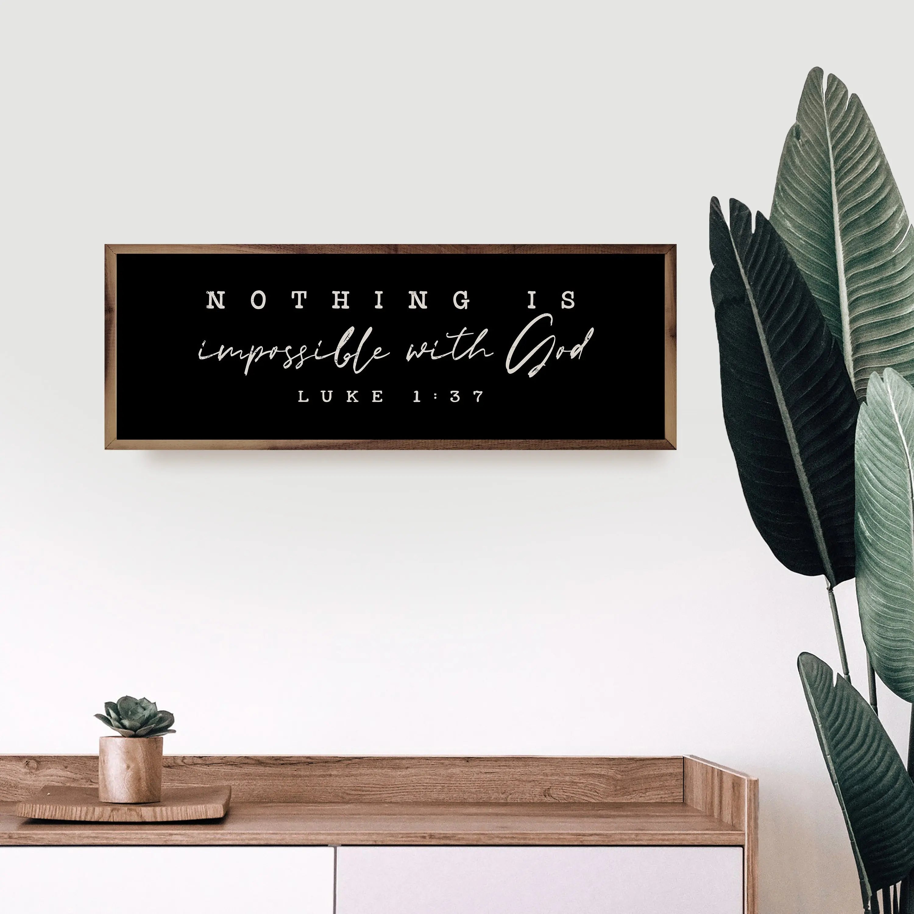 Framed quote 'Nothing is impossible with God' by Luke 1:37 on a wall above a wooden console table with plants.