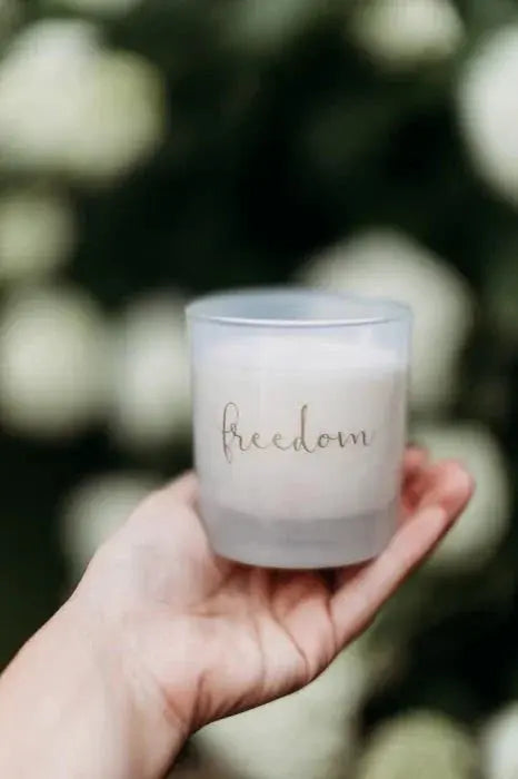 Hand holding a frosted glass candle with 'freedom' script, perfect for cozy farmhouse decor and thoughtful gifts.