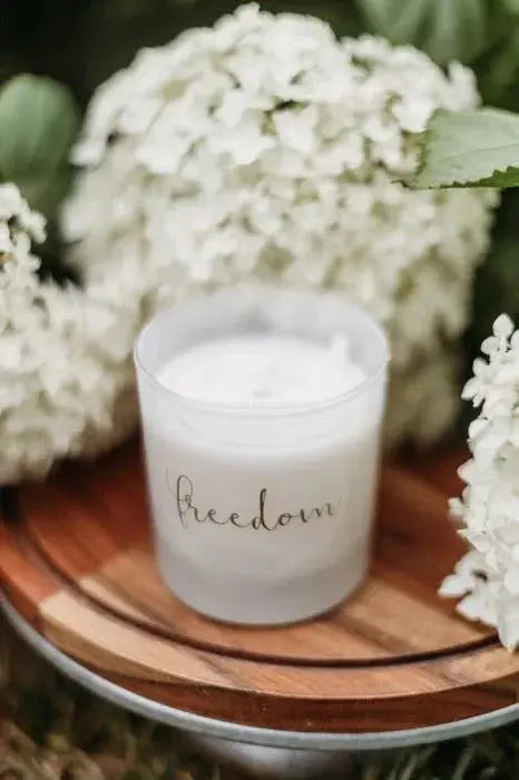 Cozy 'freedom' candle surrounded by white hydrangeas on wooden tray, farmhouse decor