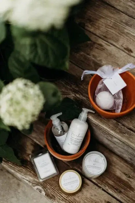 Cozy farmhouse bath essentials with candles, lotions, and bath bombs on rustic wood, styled with white hydrangeas