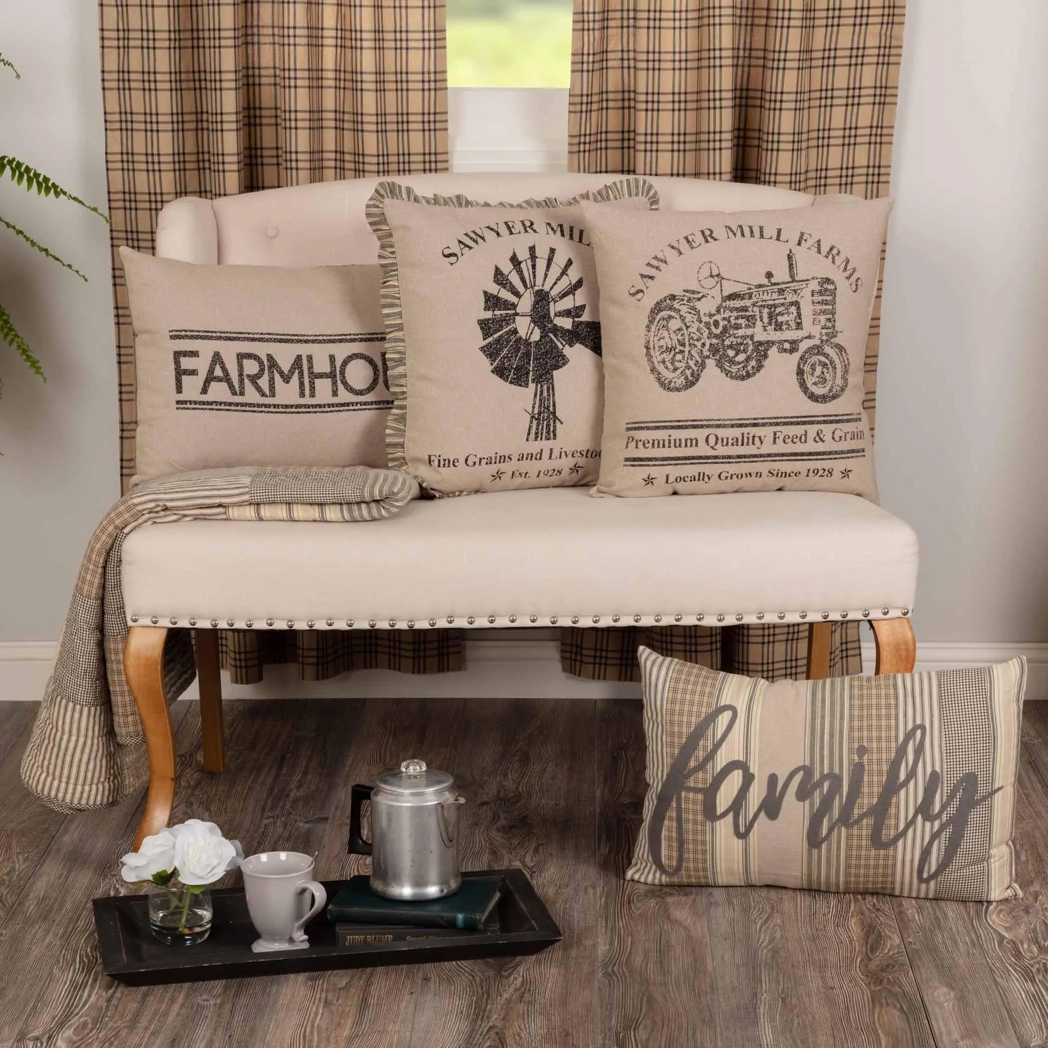 Farmhouse throw pillows with tractor, windmill, and 'family' designs on cozy bench with plaid curtains