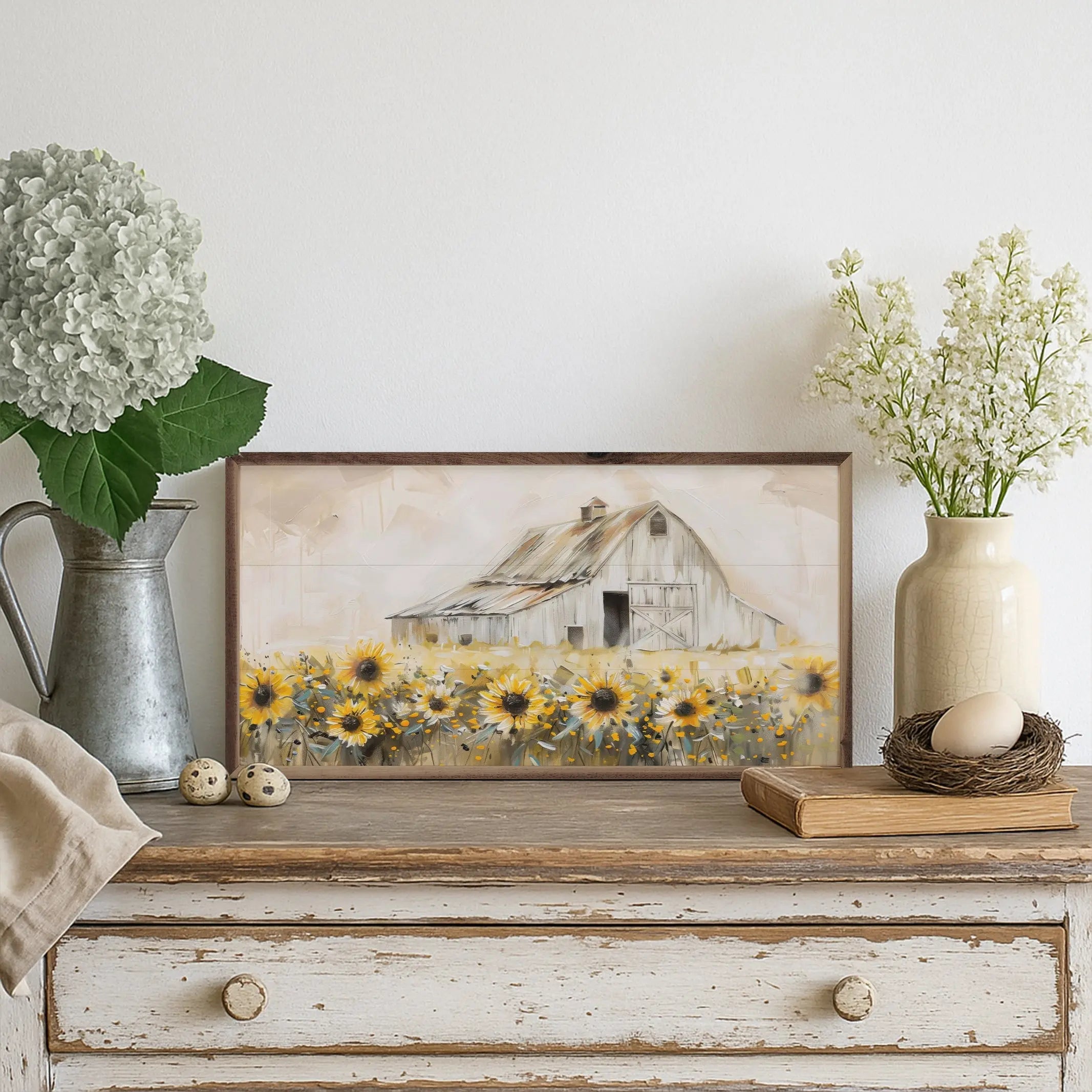 Framed artwork of a barn and sunflowers on a wooden dresser with decorative items.