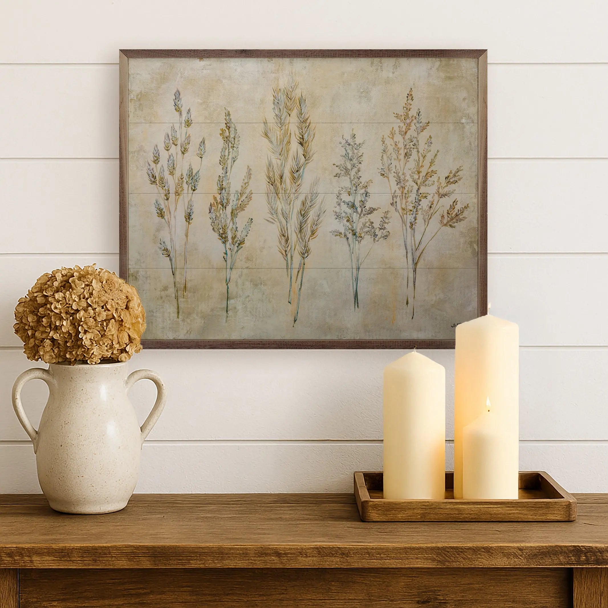 Decorative setup with a vase, candles, and framed artwork on a wooden surface.