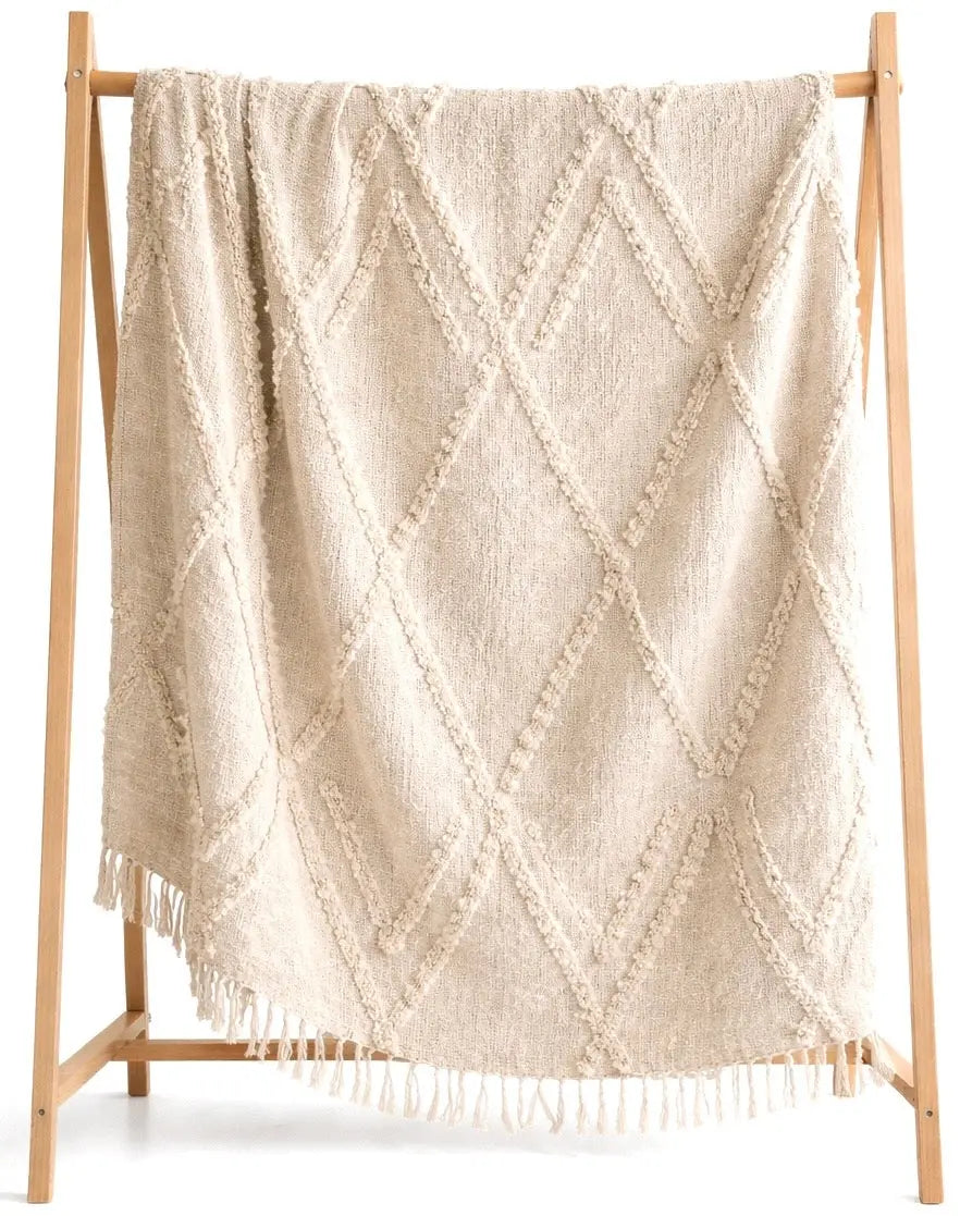 Cream diamond-patterned throw blanket with fringe, cozy farmhouse decor on wooden stand