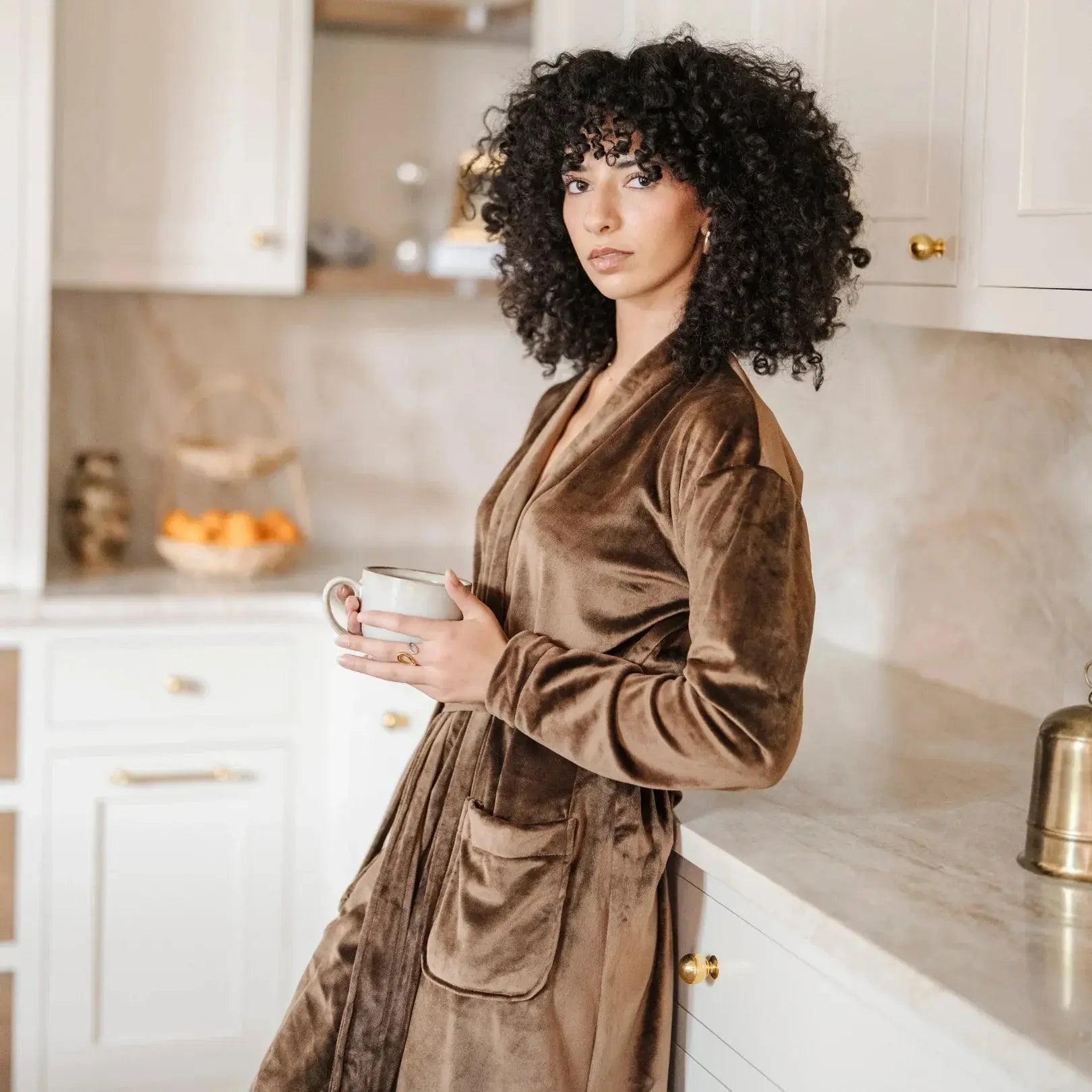 Woman in cozy brown velvet robe holding mug in farmhouse kitchen, warm home decor vibe