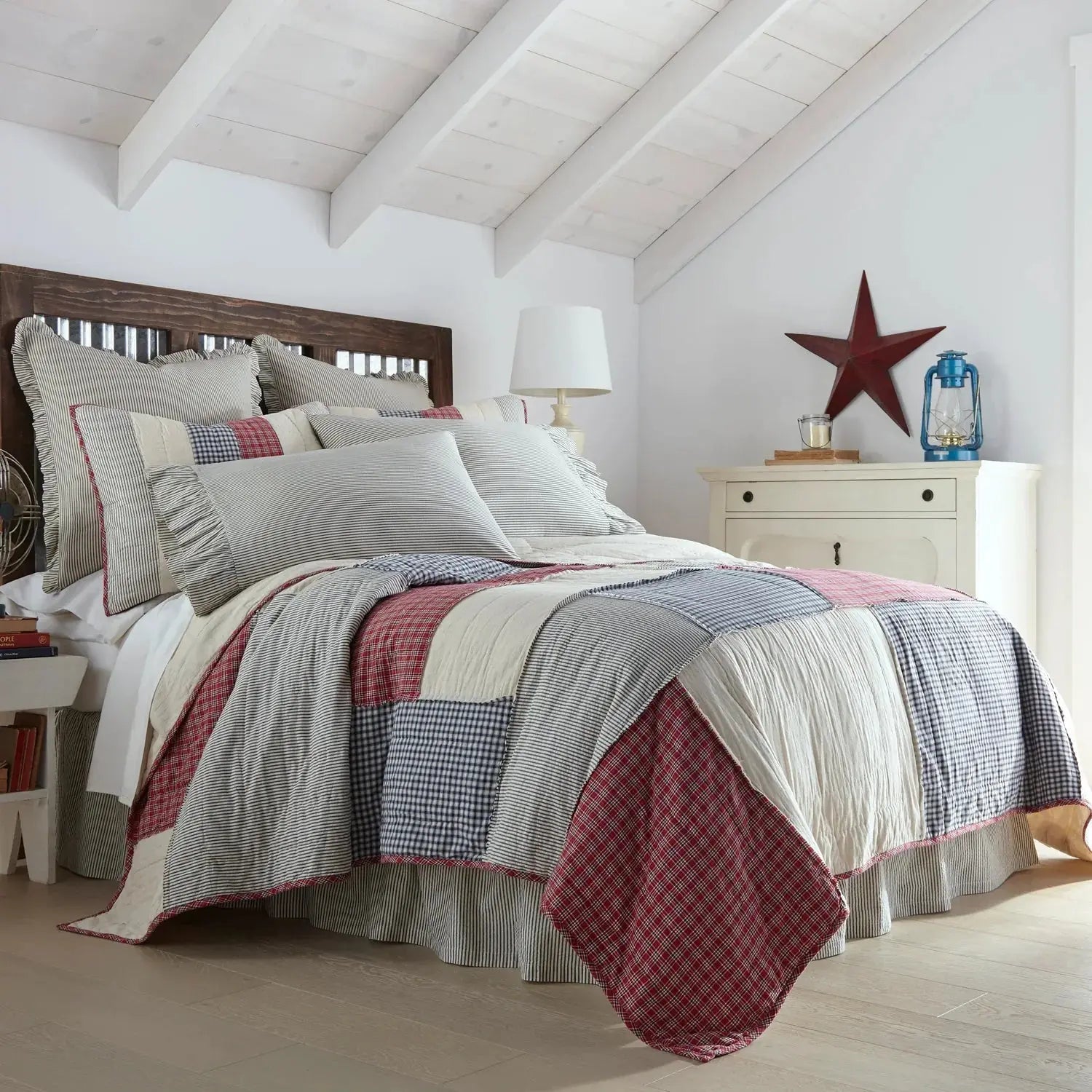 Cozy farmhouse patchwork quilt set with red, blue, and white plaid patterns in a rustic bedroom