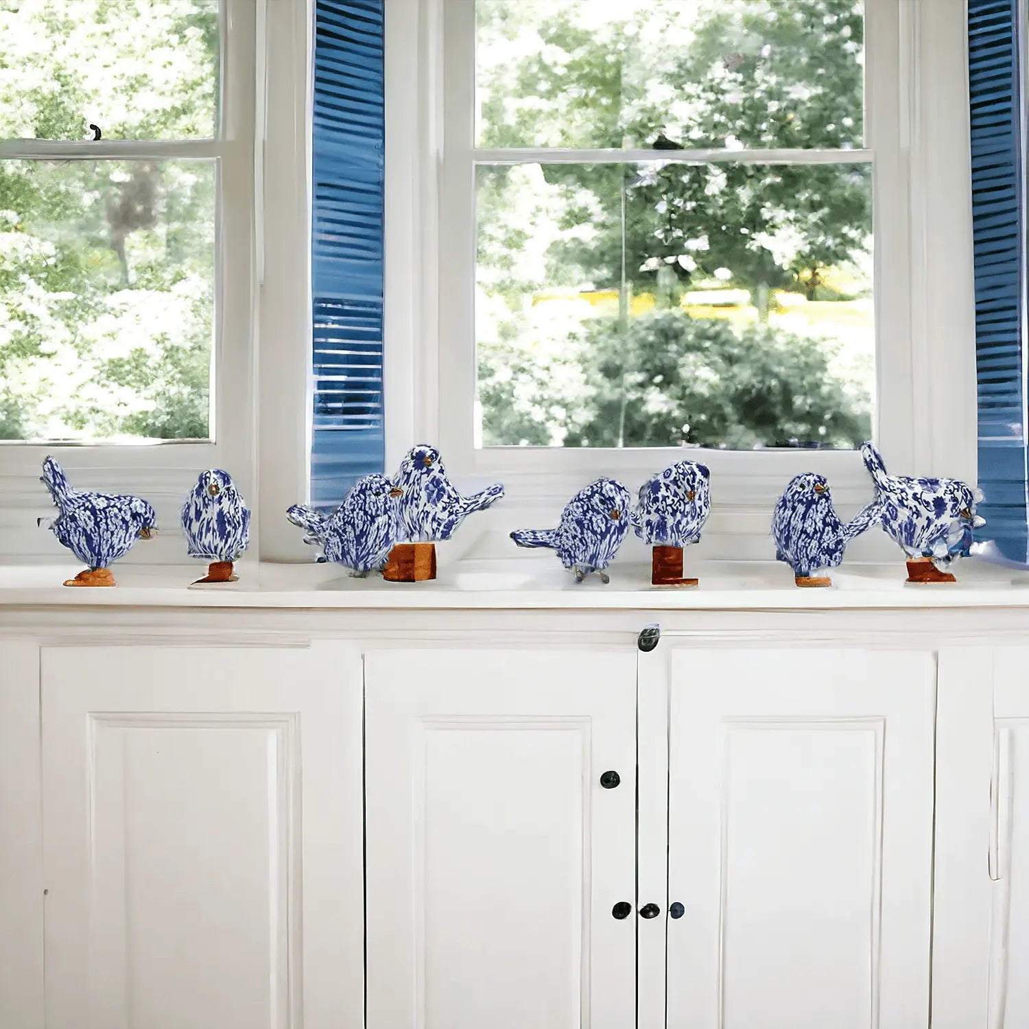 Decorative blue and white ceramic birds on a windowsill with a white cabinet below.