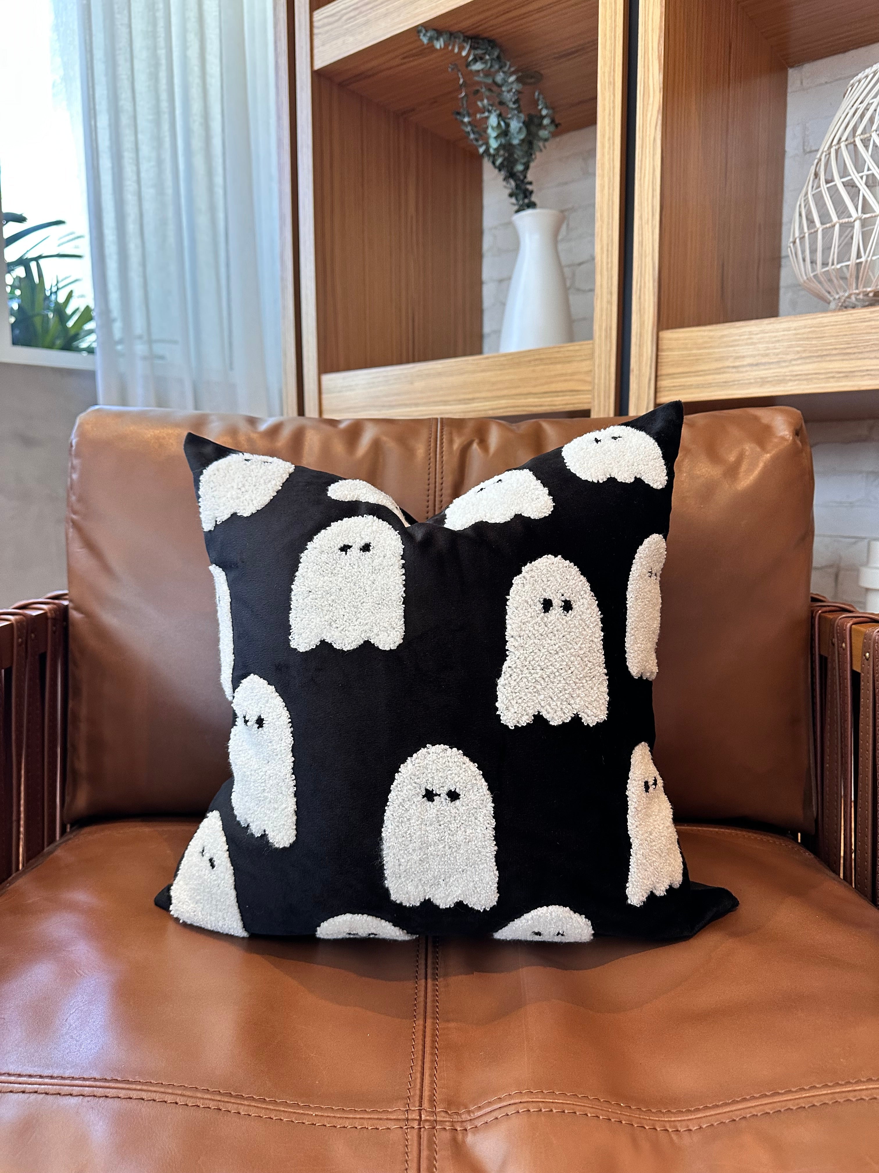 Black pillow with white ghost patterns on a brown leather chair