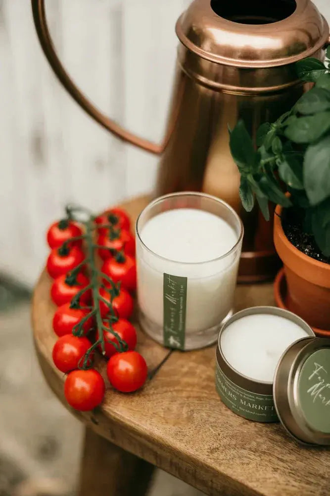 Farmers Market scented candle with cherry tomatoes, basil plant, and copper pitcher on rustic wood table