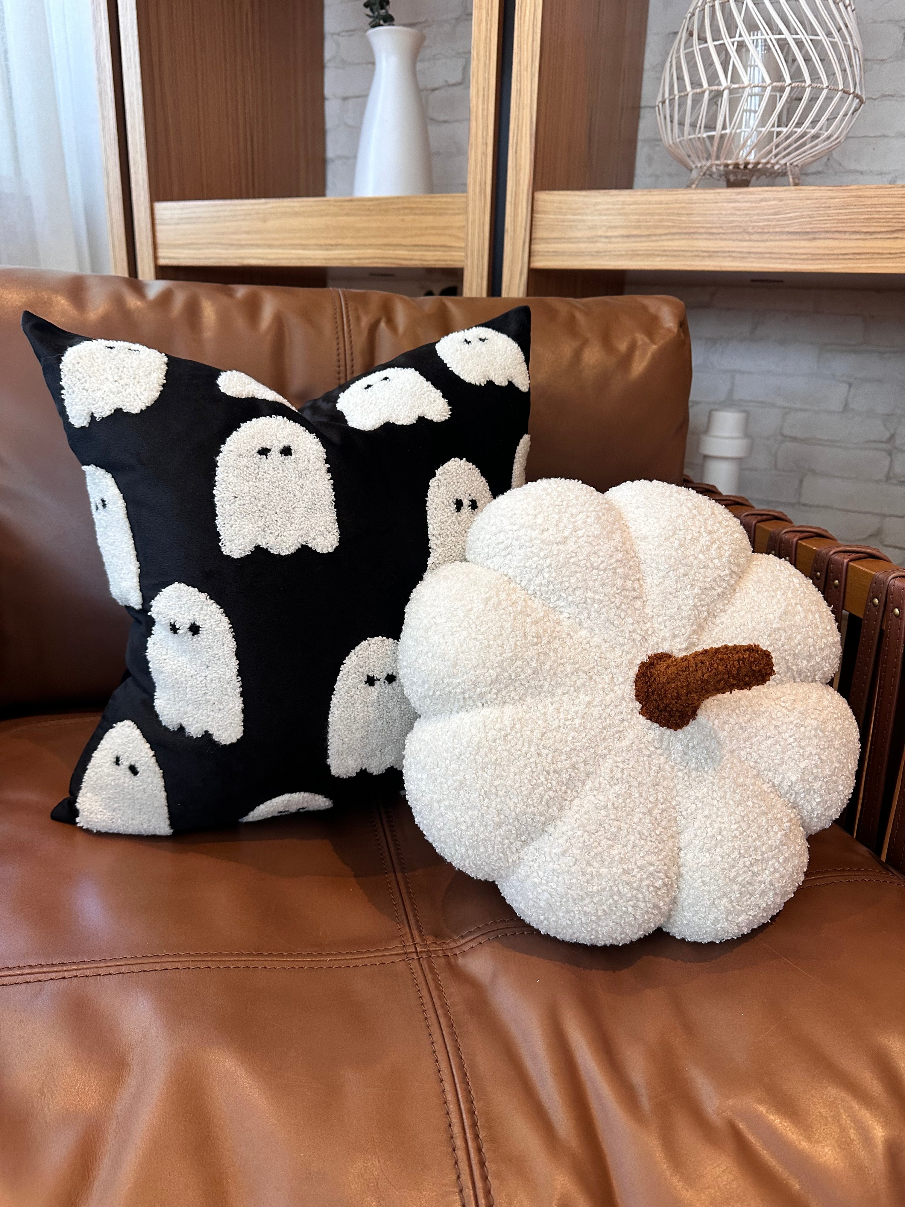 Decorative pillow with ghost pattern and pumpkin-shaped pillow on a brown leather couch.