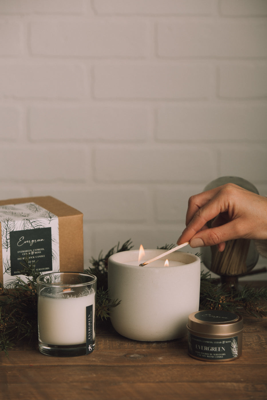 Person lighting a candle with a wooden wick trimmer on a wooden surface.