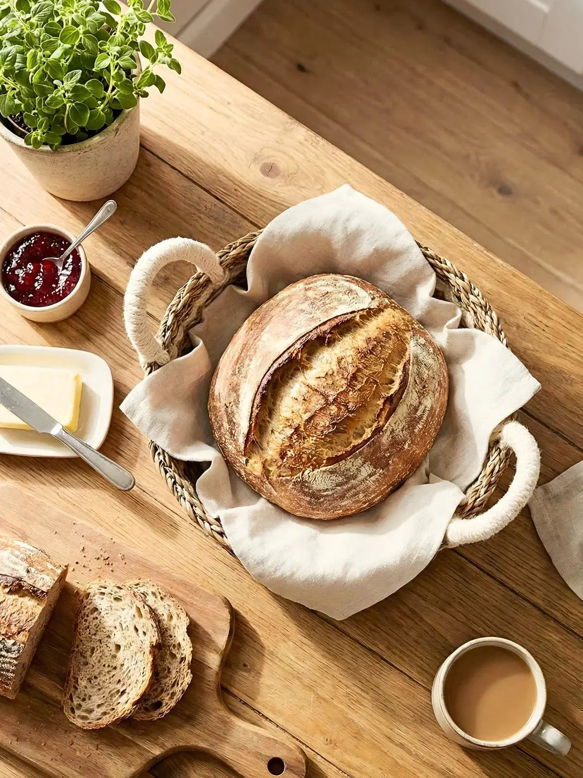 Freshly baked sourdough bread in a wicker basket with jam, butter, and coffee on a rustic wooden table