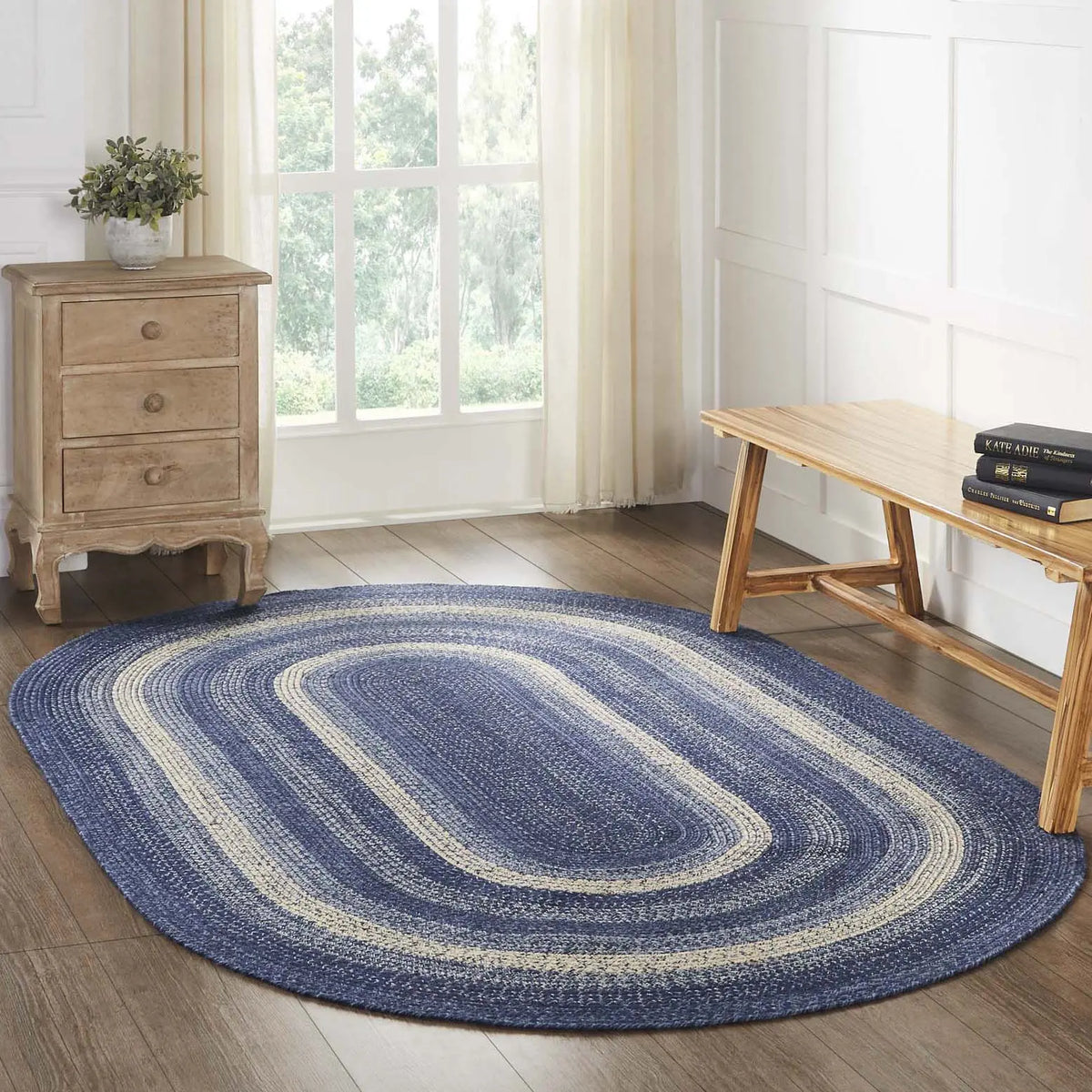 Blue oval braided rug in a room with wooden furniture and a window.