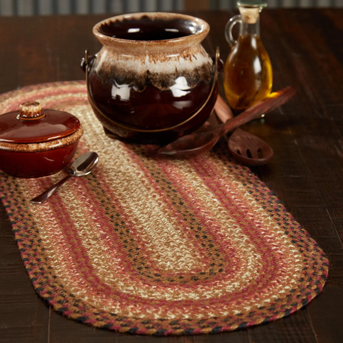 Ceramic pot, wooden spoon, and glass container on a woven placemat with a striped background.