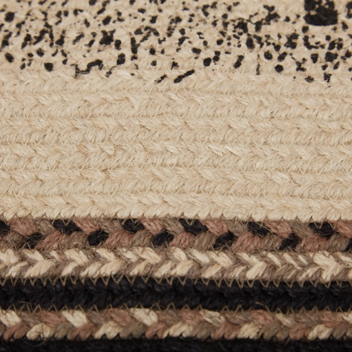 Close-up of a braided rug showing a cream base with black speckled detailing, a woven beige and brown stripe, and dark brown braided bands.