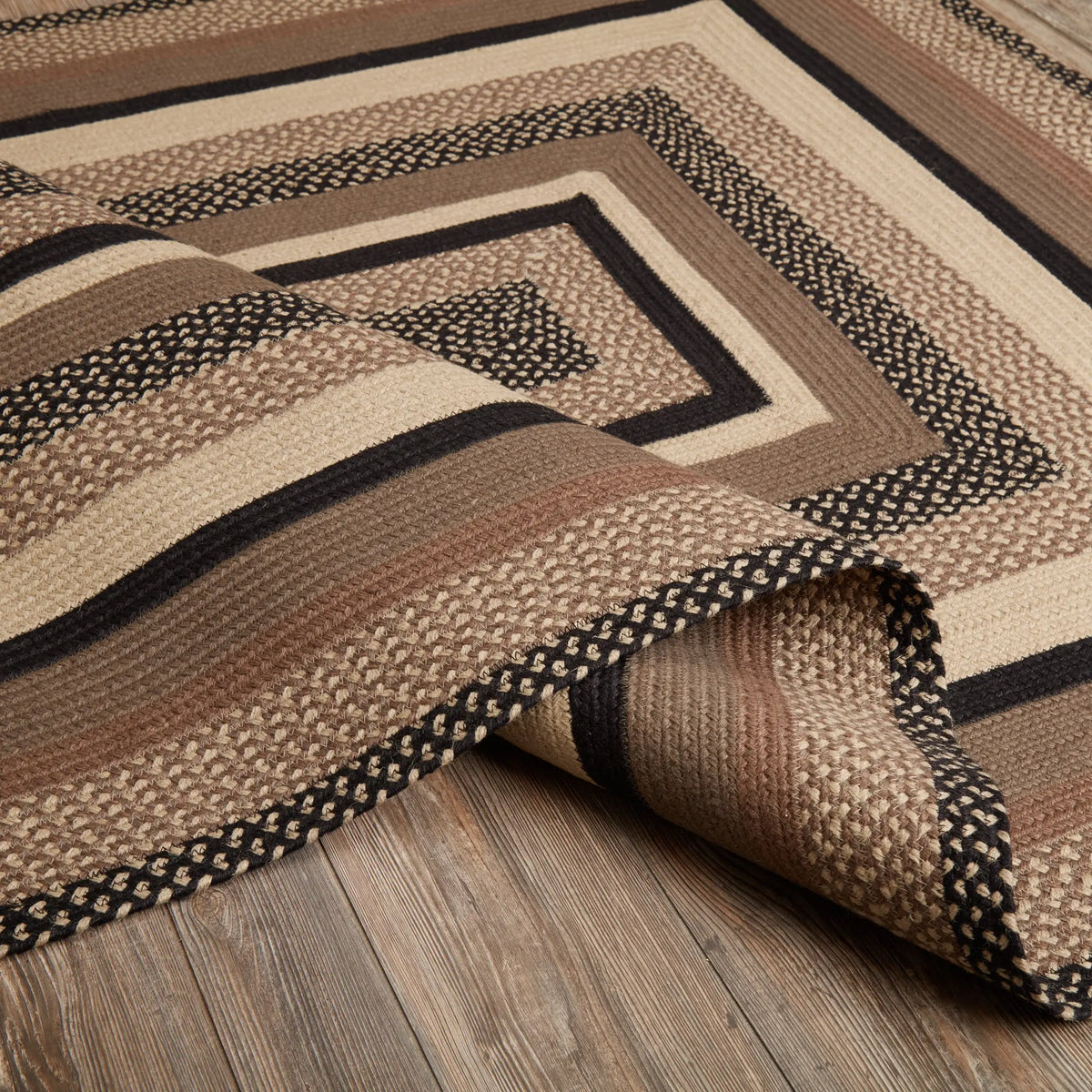 A close-up of a woven area rug with a geometric pattern in beige, brown, and black, draped over a rustic wood floor.