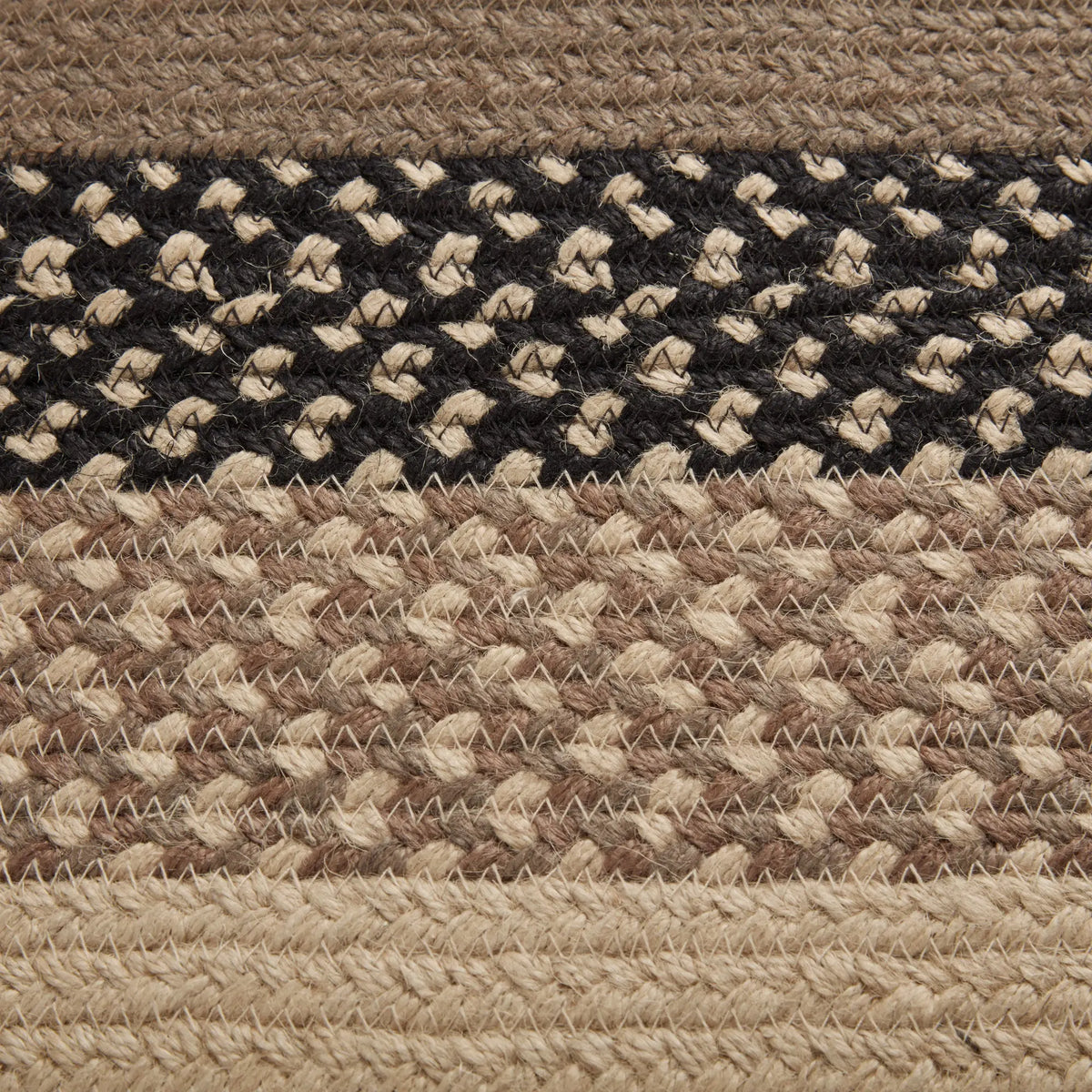 Close-up of a braided woven rug with horizontal bands in beige, black, and mixed brown and beige patterns.