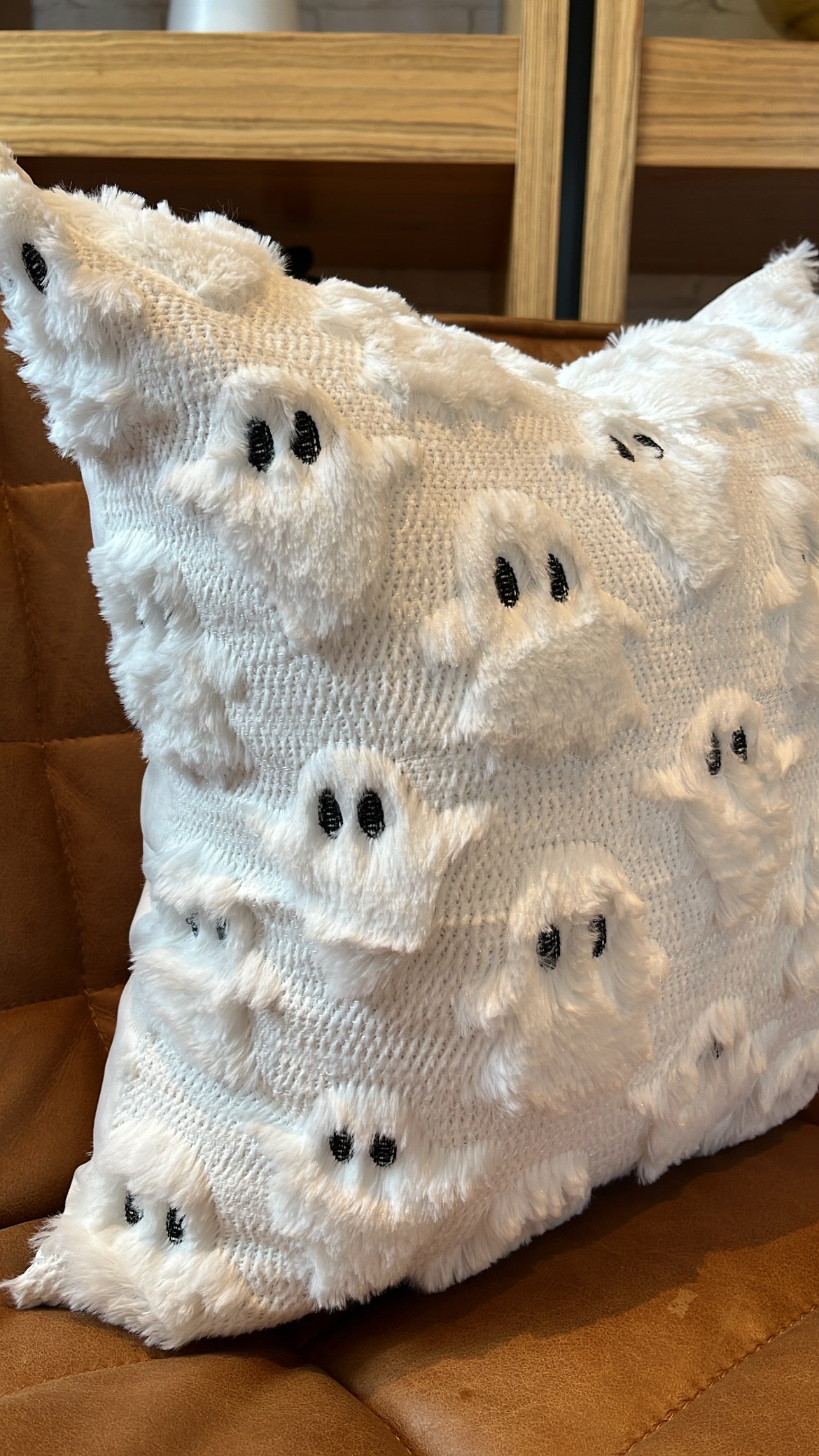 White knitted pillow with black button eyes on a brown surface