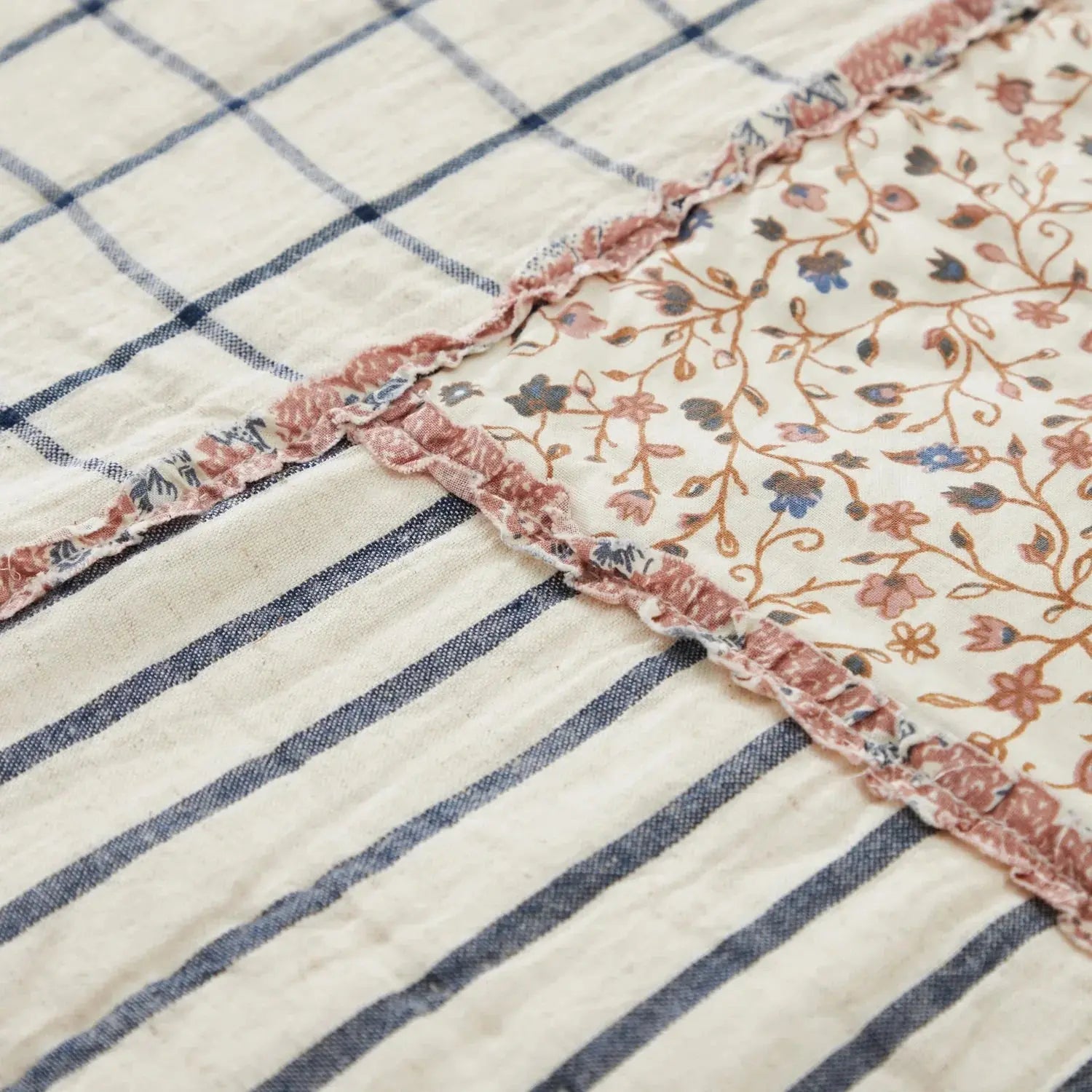 Cozy farmhouse quilt with blue stripes, floral patch, and ruffled trim for cottage-style home decor