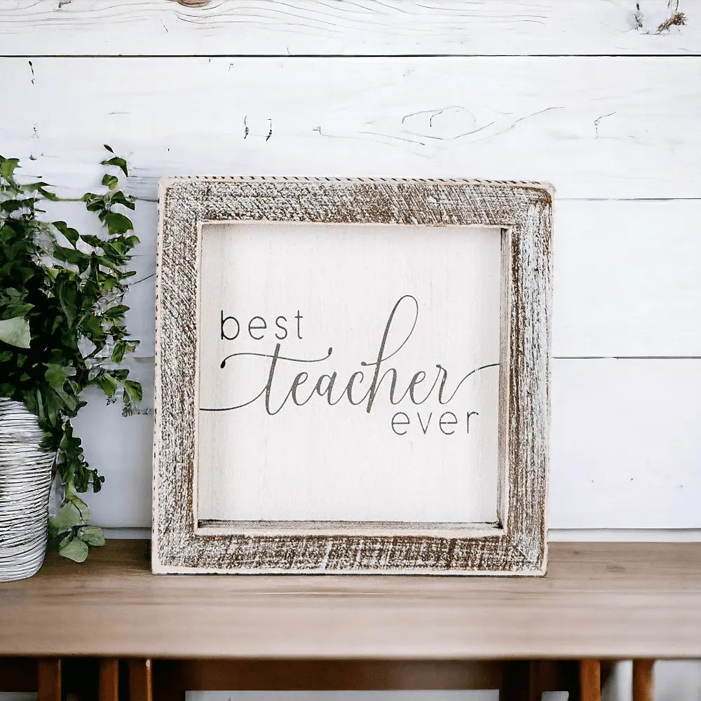 Decorative sign with 'best teacher ever' text in a rustic frame on a wooden surface.