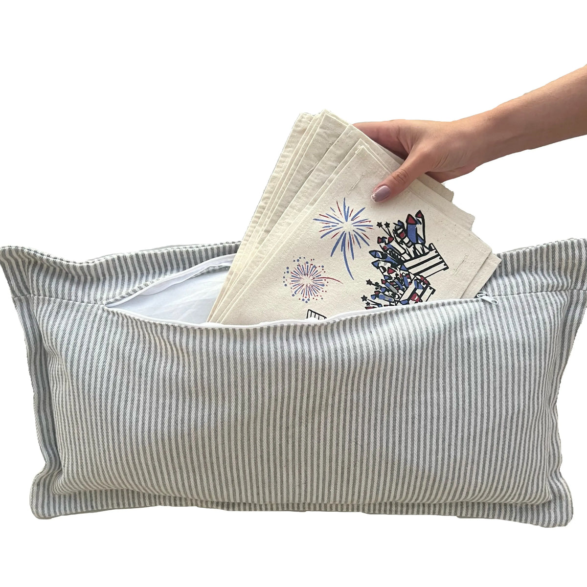 A striped fabric storage bin or pouch with a hand reaching in to pull out folded embroidered napkins or cloths showing colorful floral and fireworks designs.