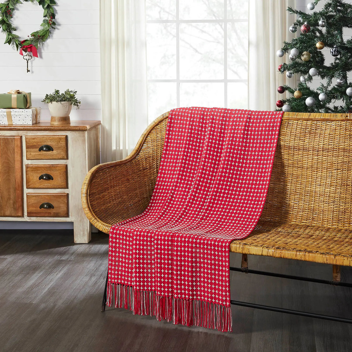 Red checkered throw blanket draped over a wicker chair in a room with Christmas decorations.
