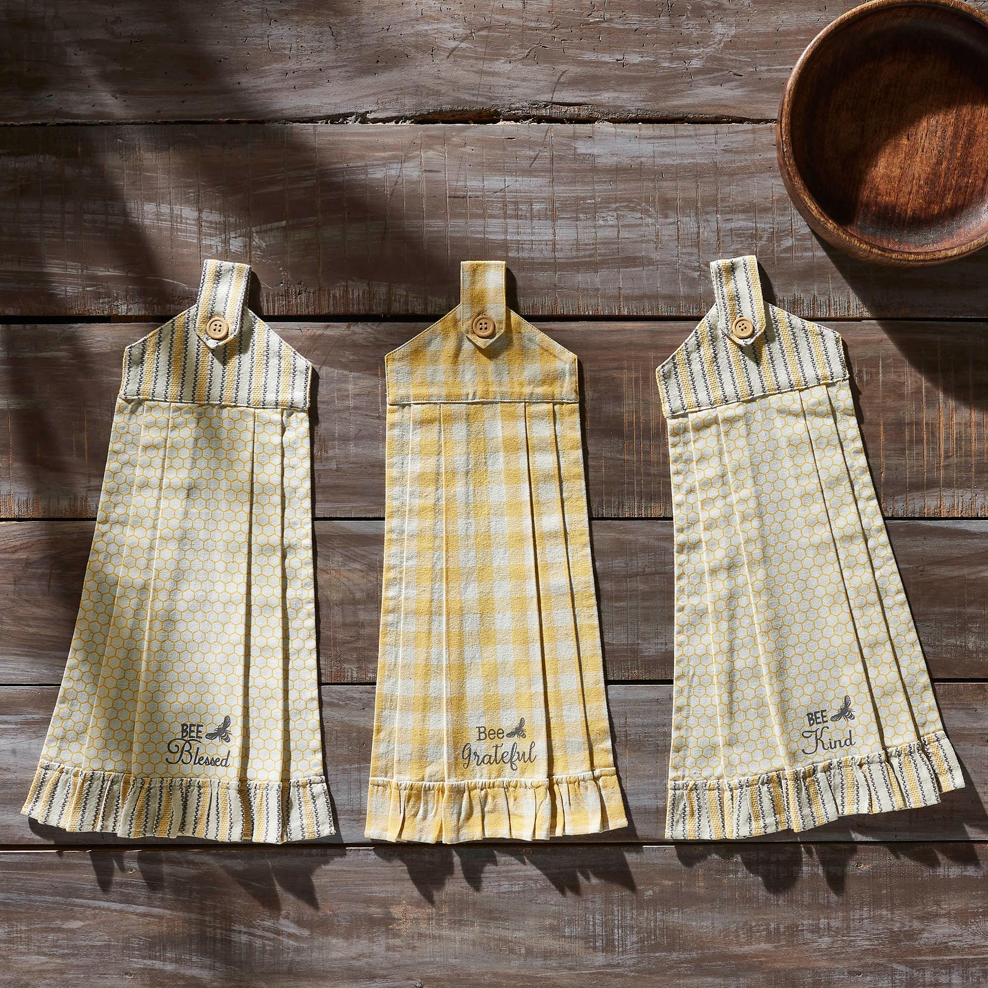 Yellow and white farmhouse kitchen towels with bee quotes, honeycomb patterns, and ruffled edges on rustic wood.