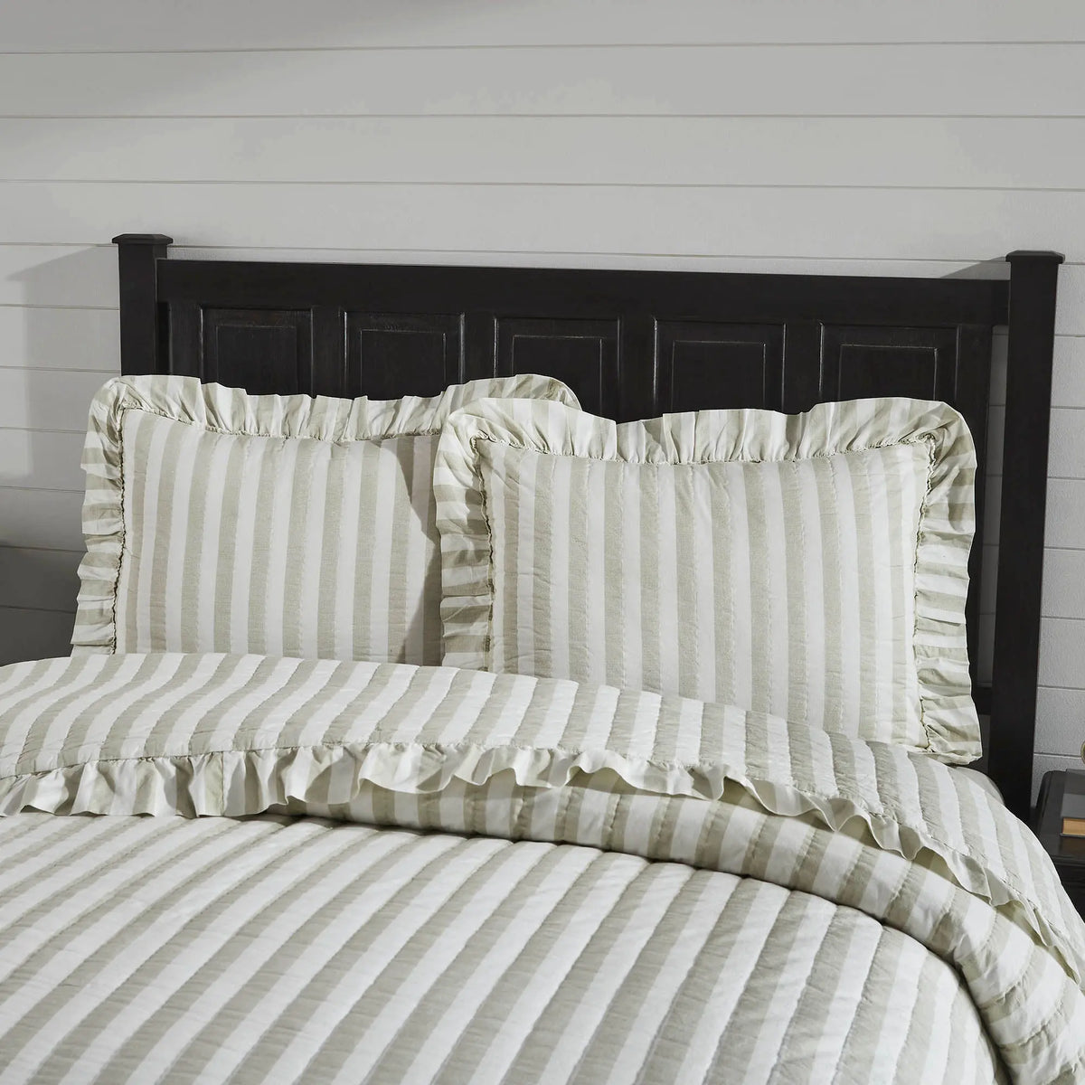 Striped bedding with ruffled edges on a bed with a wooden headboard.
