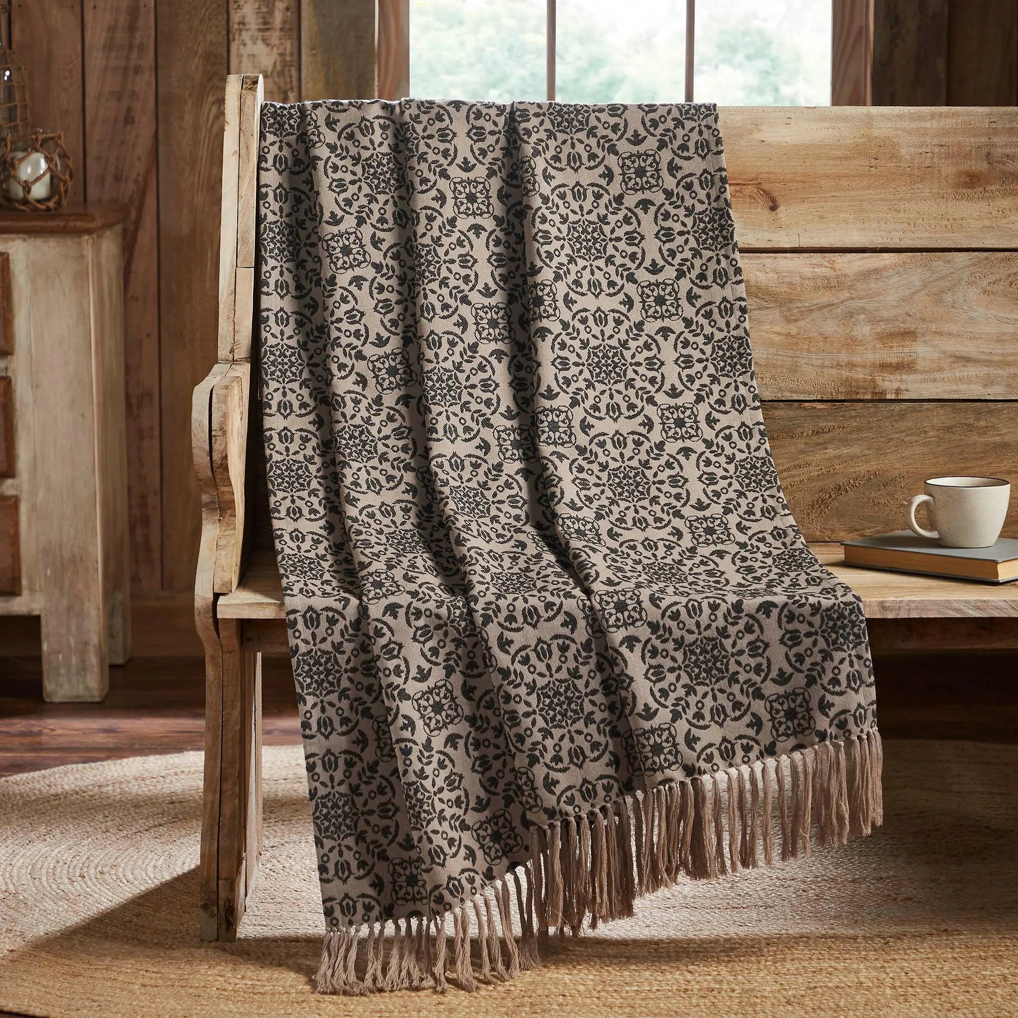 Cozy farmhouse throw blanket with black floral pattern and fringe, draped on rustic wooden chair