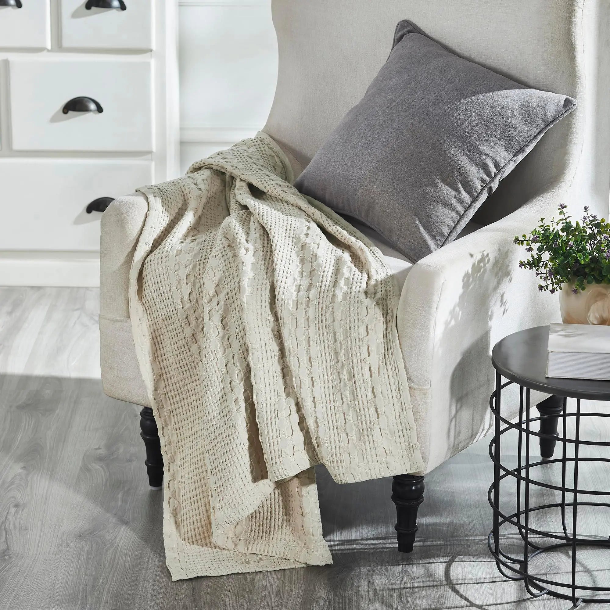 Cozy farmhouse armchair with gray pillow, cream waffle knit throw blanket, and side table with plant