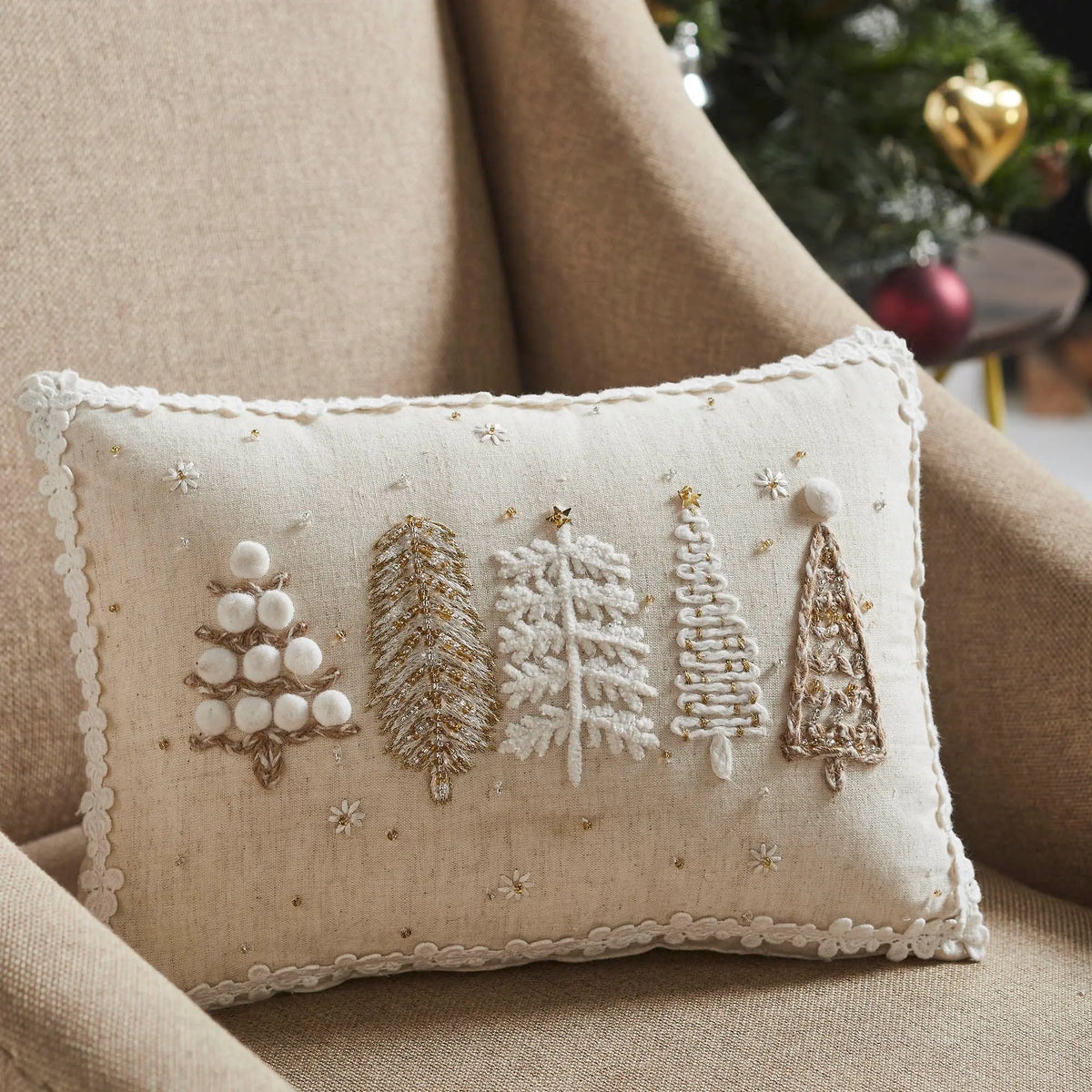 Decorative pillow with embroidered trees on a beige couch.