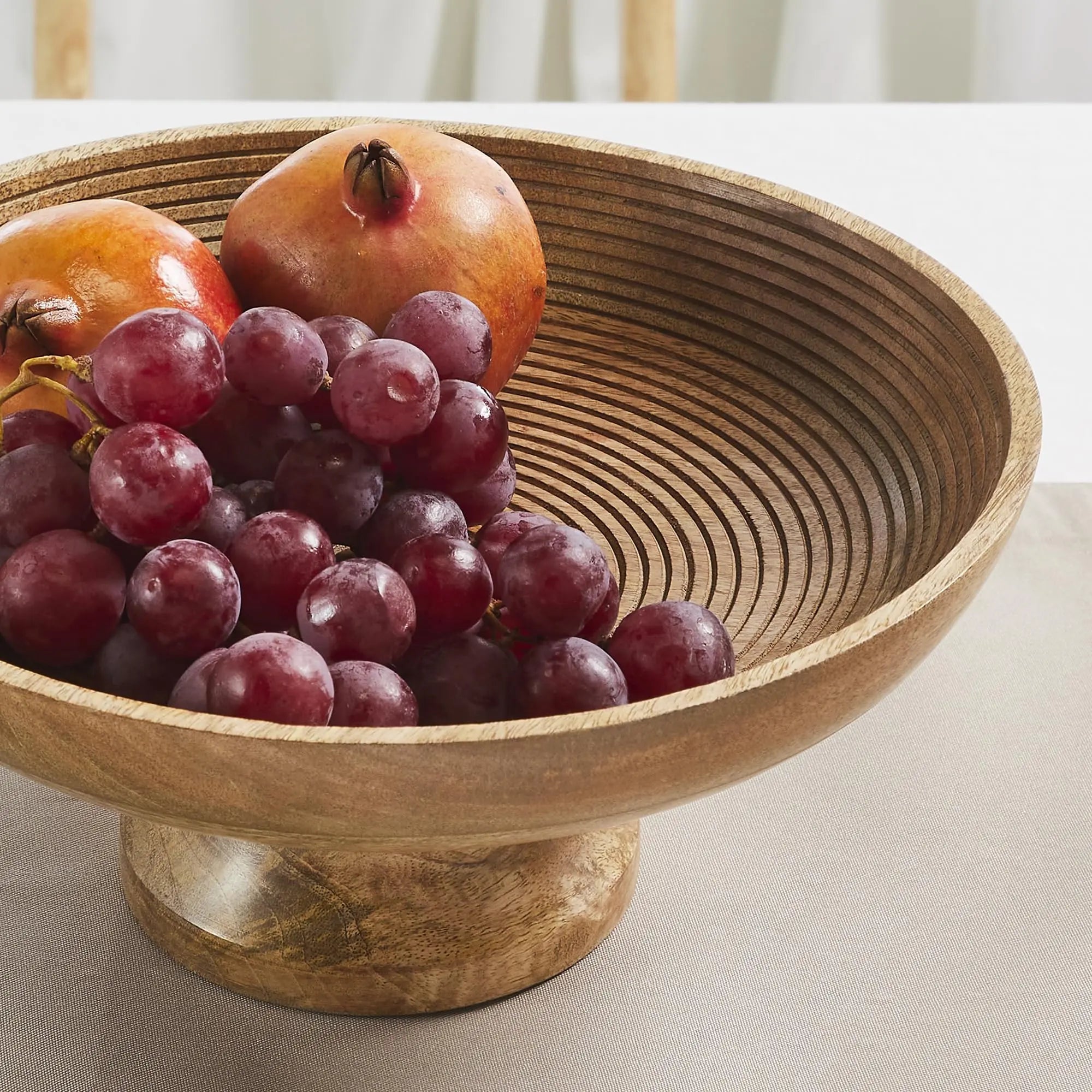 Wooden bowl with grapes and pomegranates on a light surface
