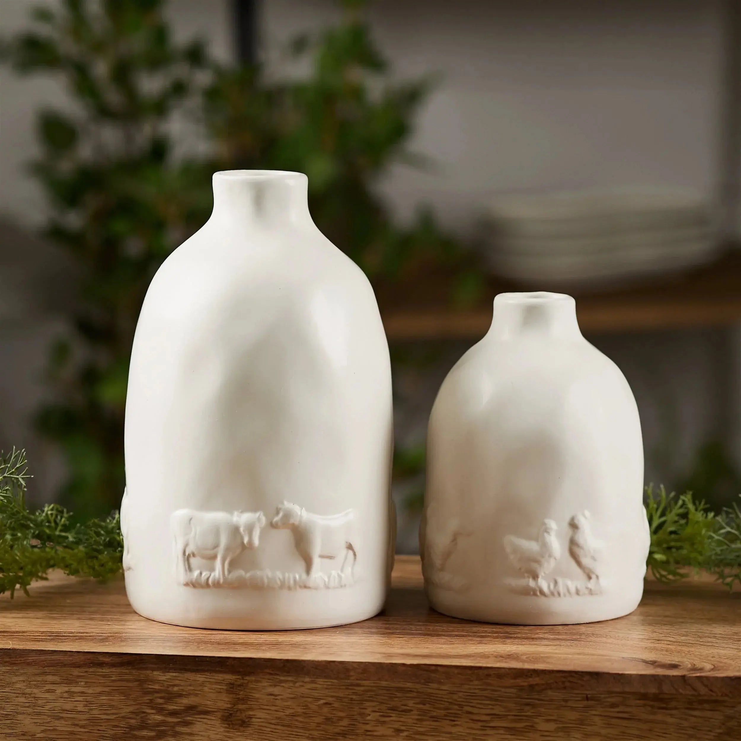 Two white ceramic bottles with embossed designs of animals on a wooden surface.