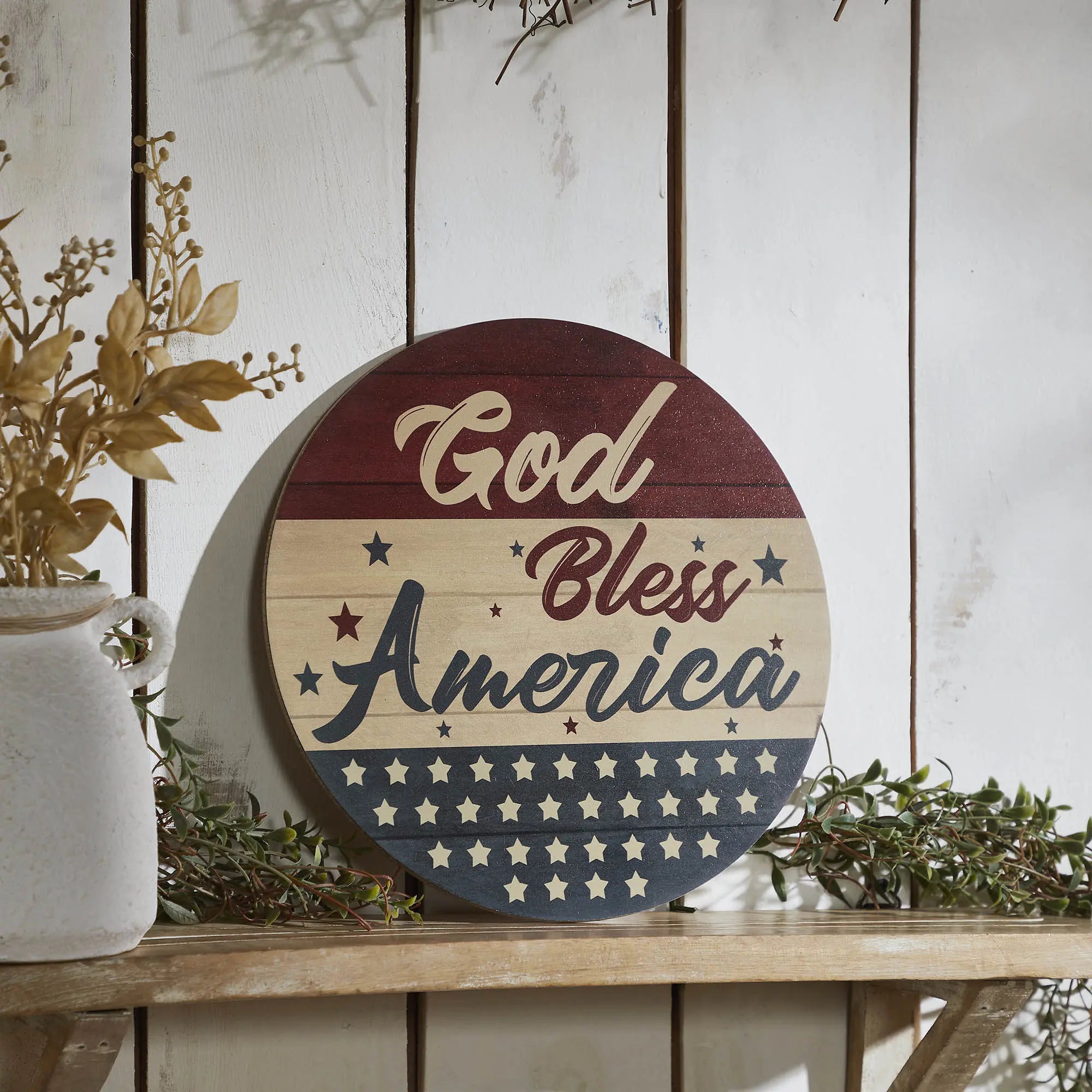 Decorative sign with 'God Bless America' text on a wooden surface with plants.