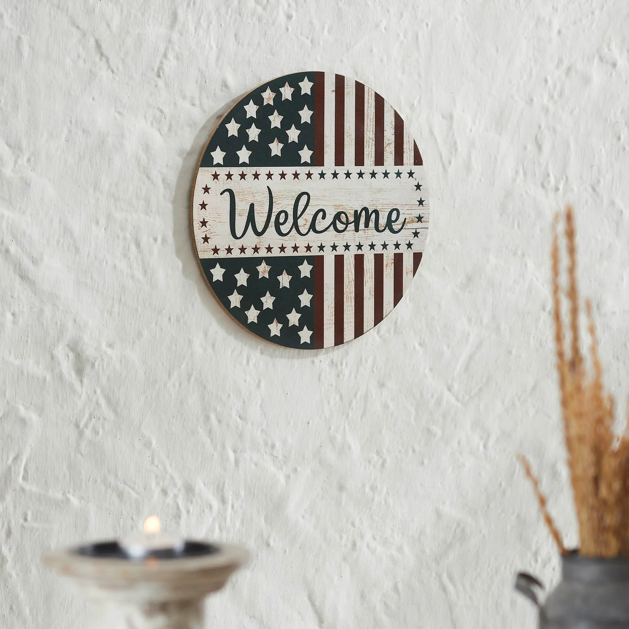 Round wooden sign with American flag design and 'Welcome' text on a white wall.