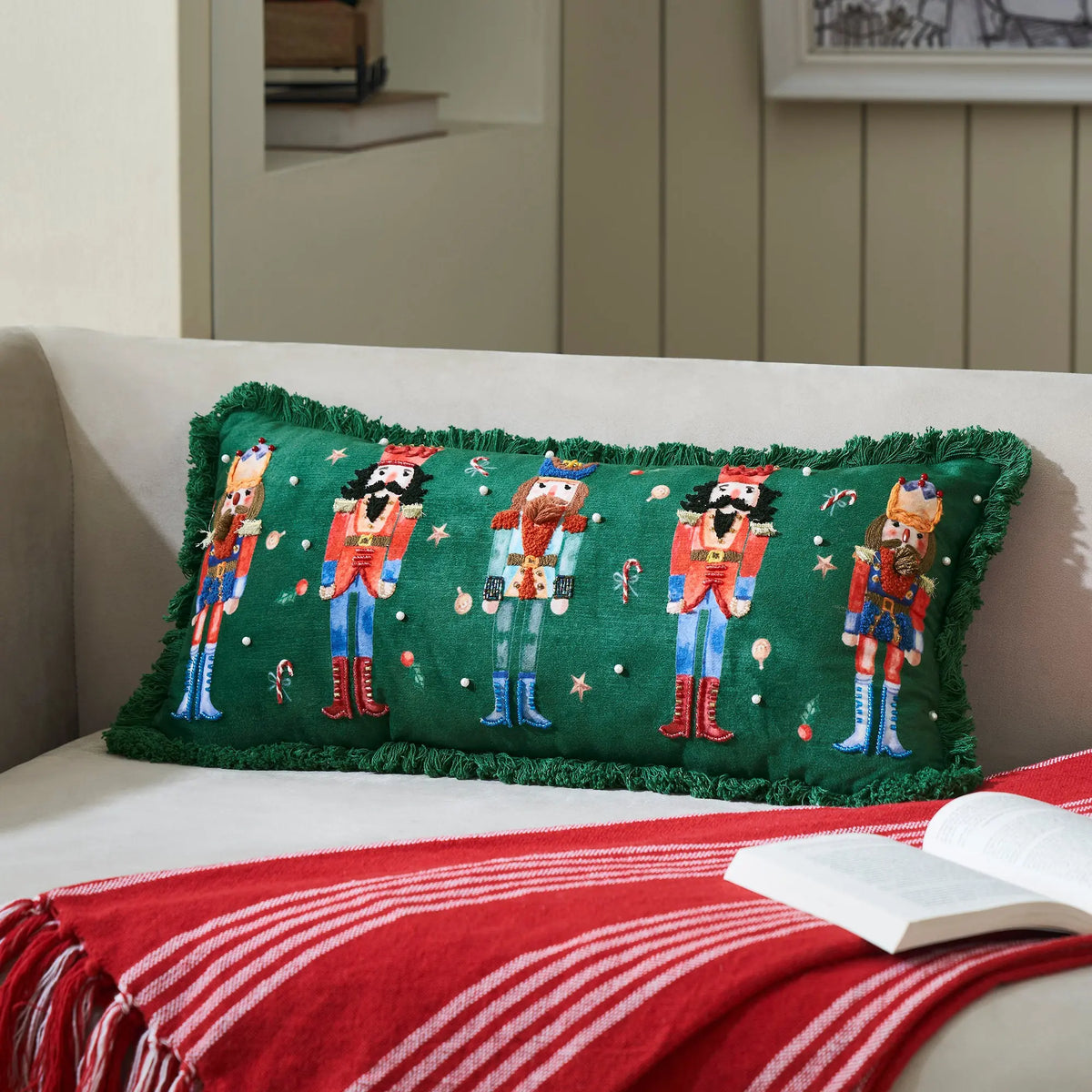 Decorative pillow with nutcracker design on a couch with a red blanket and book.