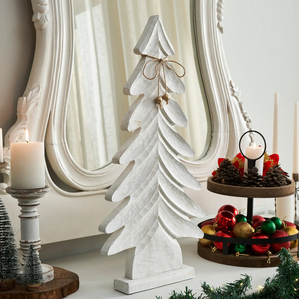 Decorative white Christmas tree with candles and ornaments on a mantelpiece.