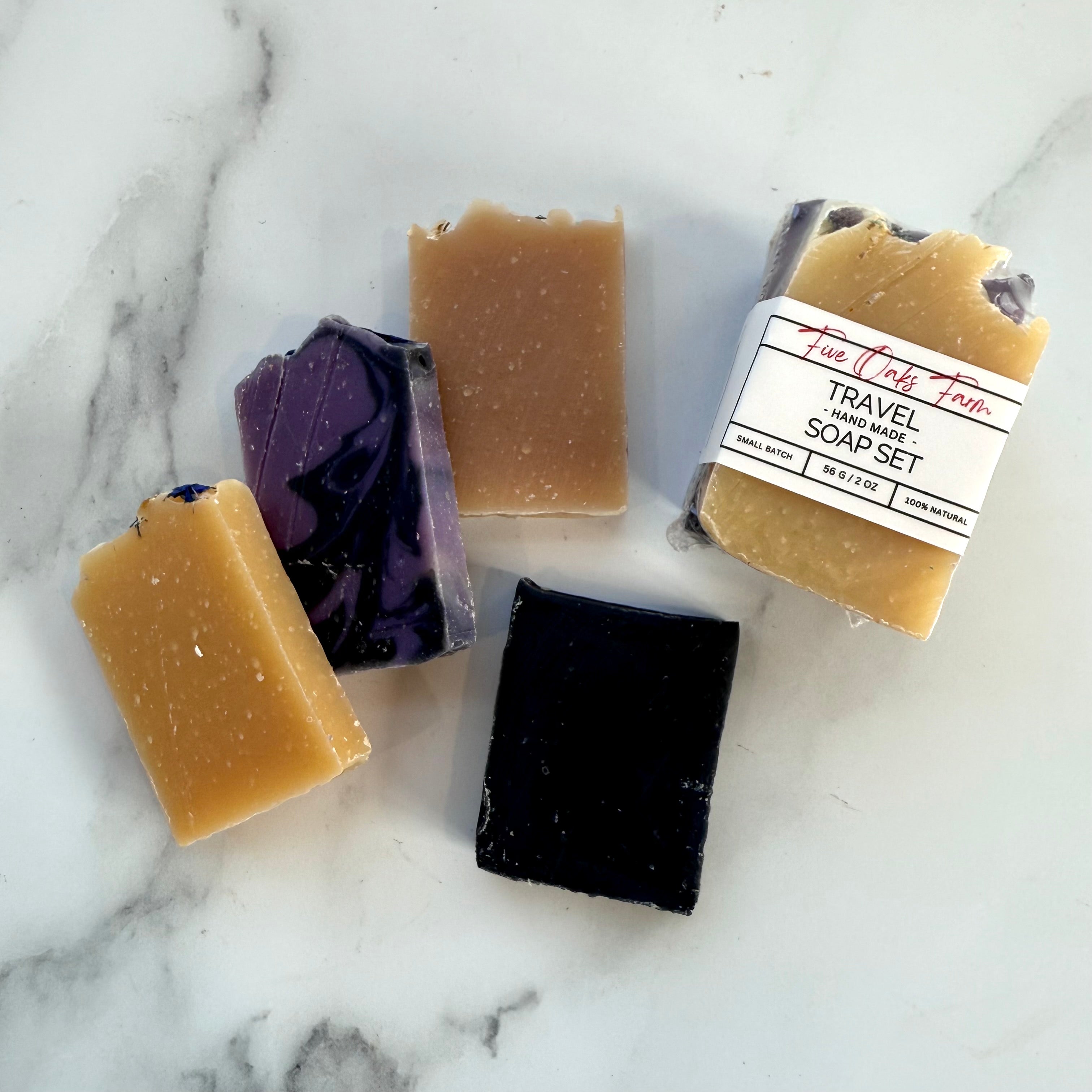 Five handmade soap bars on a marble surface with a label indicating 'Travel Handmade Soap Set'.